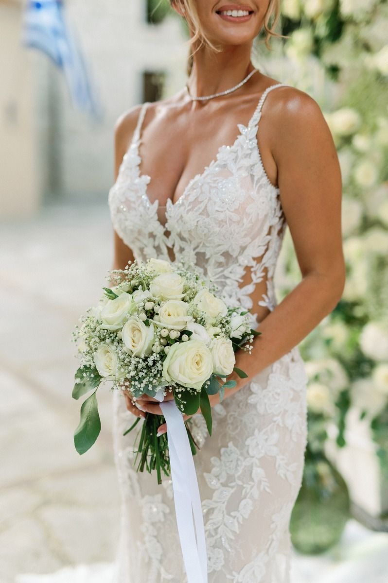 Close-up of lace wedding dress with white rose bouquet featuring delicate floral details.