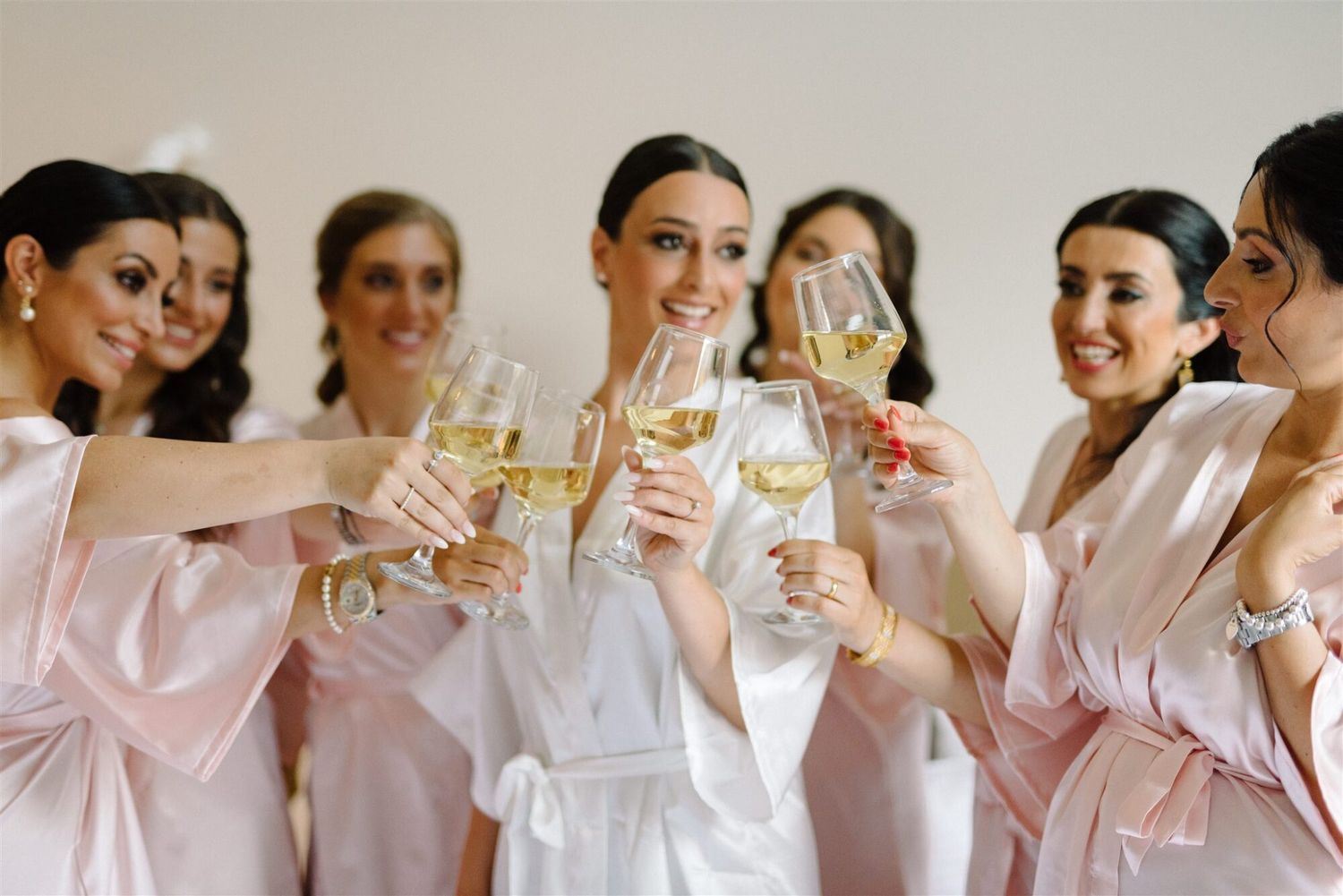 Group wearing matching blush pink robes sitting together on a couch with champagne glasses.