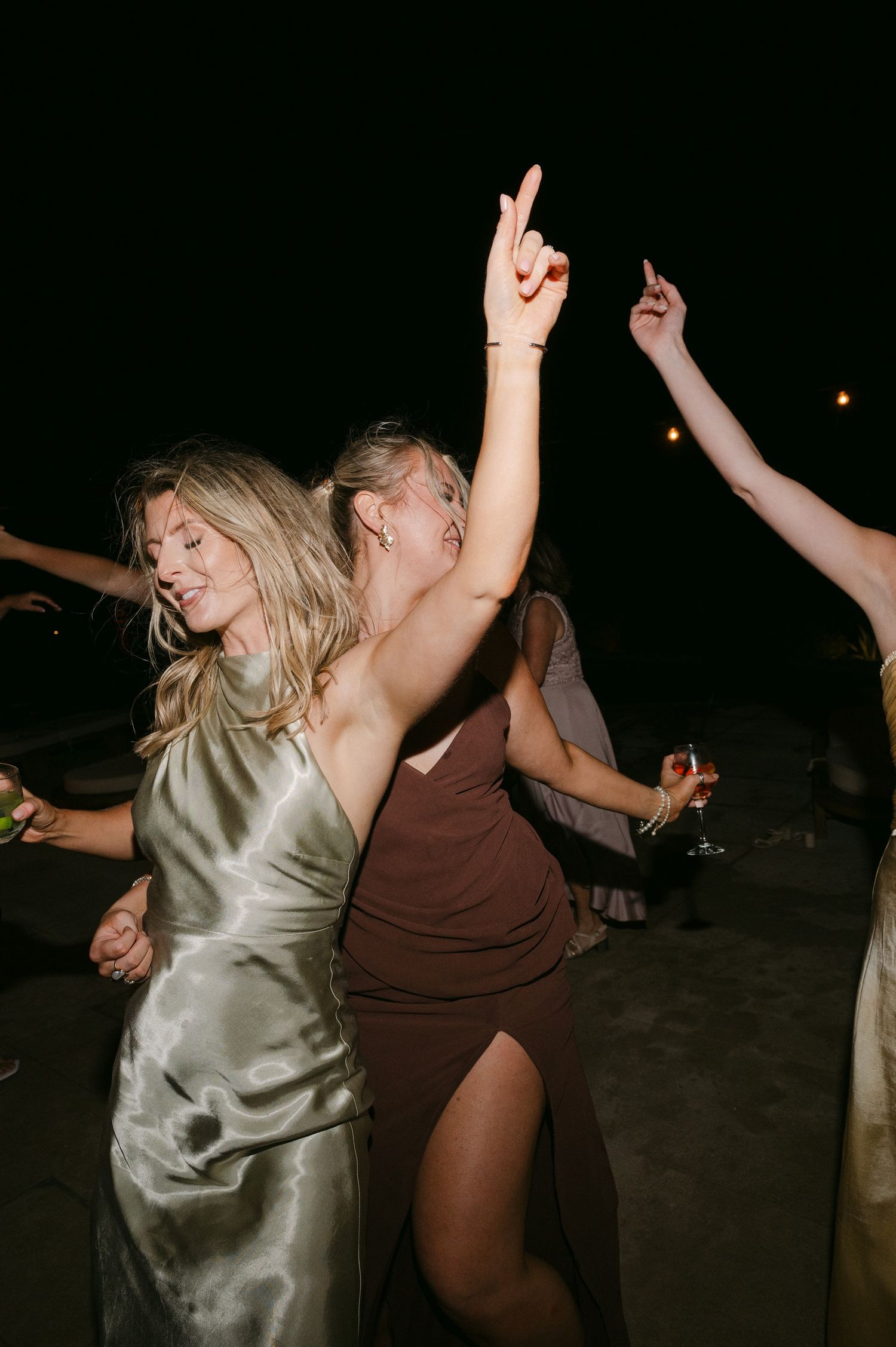 Two people dancing energetically in a dark room, one wearing a silver dress and another in brown clothing.