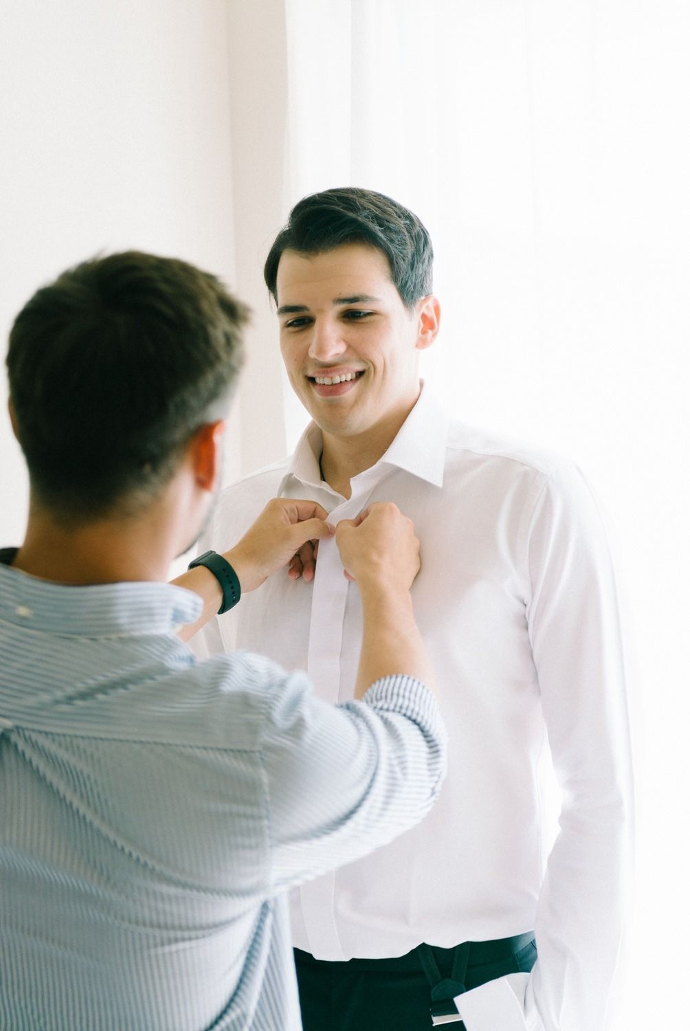 Getting help with buttoning up a crisp white dress shirt in preparation for a formal event.