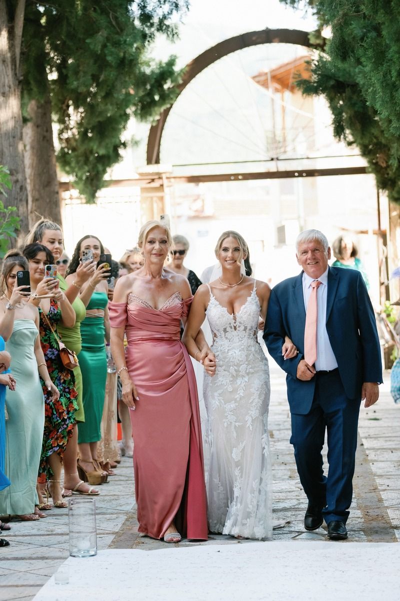 Wedding party processional walking down stone path under archway as guests look on.