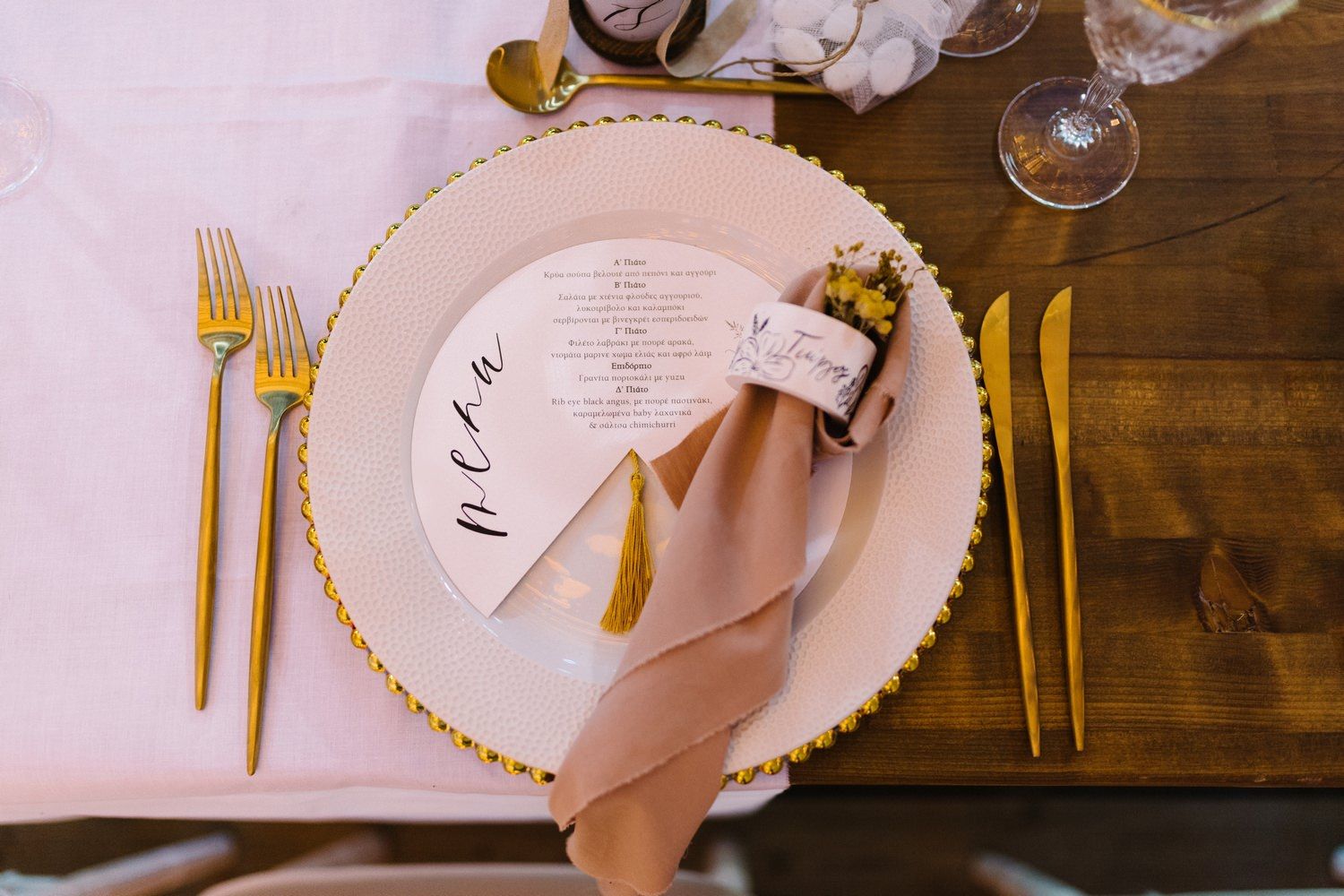 Elegant place setting with gold cutlery, pink napkin and gold-rimmed charger plate.