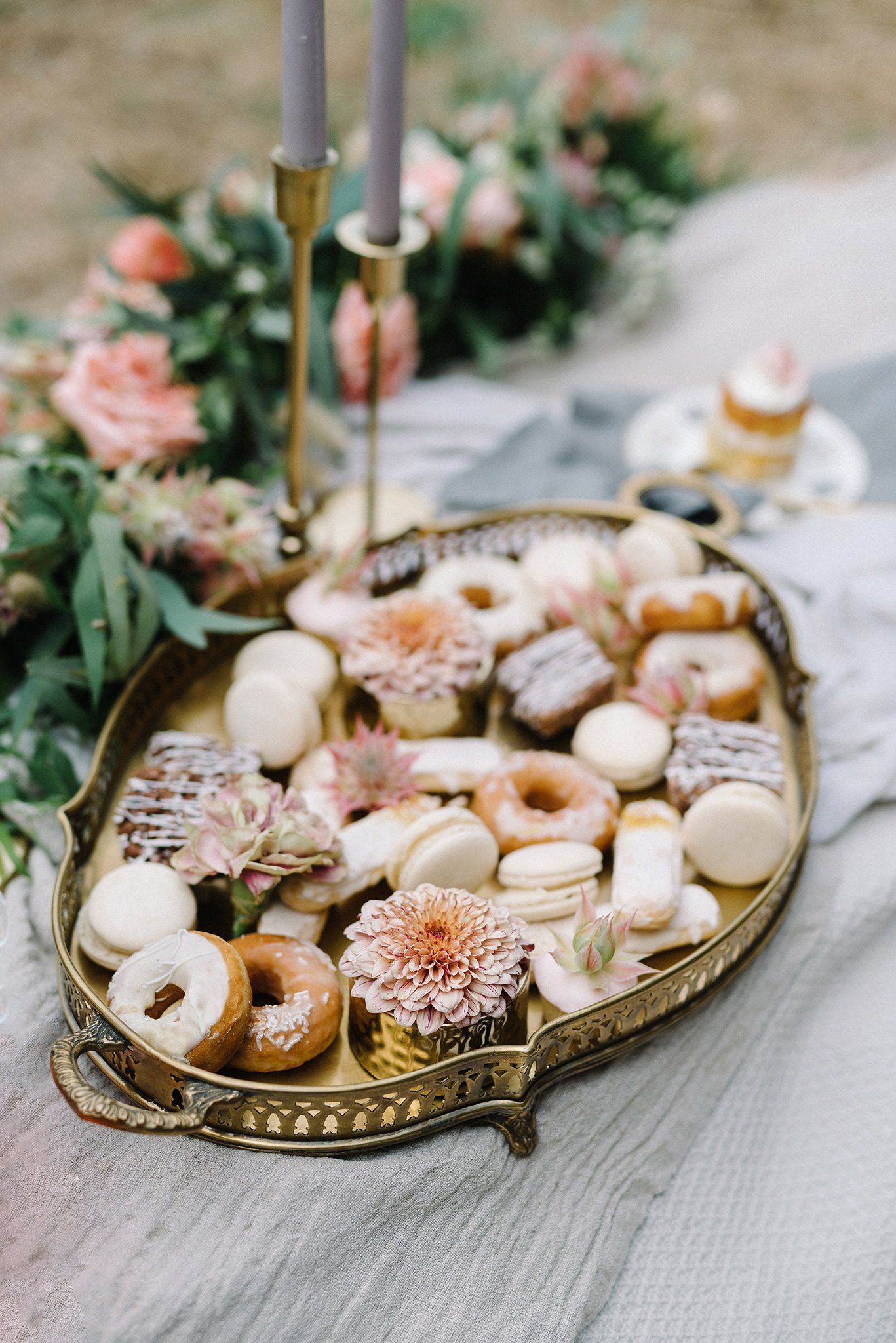 Elegant dessert platter with macarons, donuts and flowers on vintage gold tray.