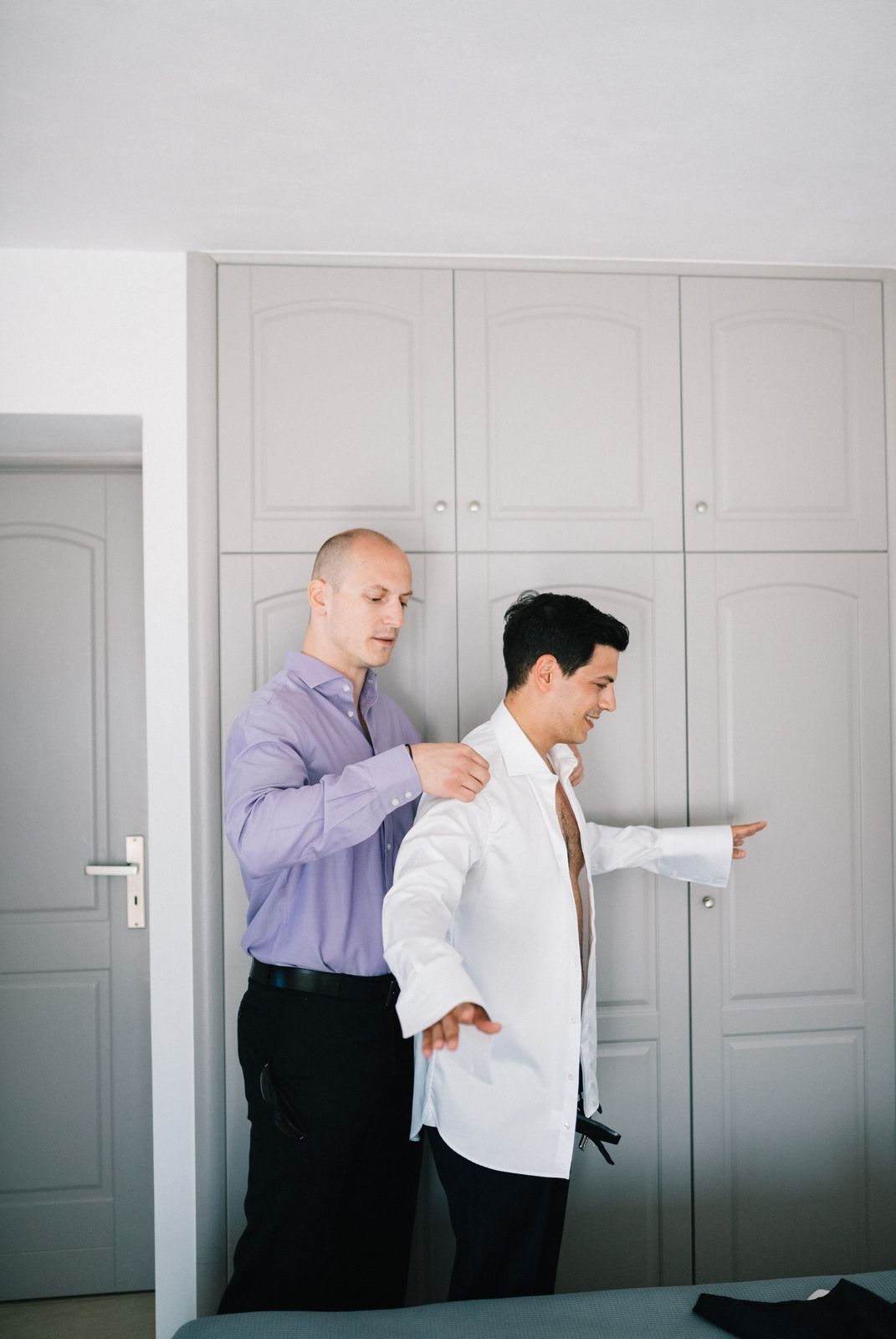Two people in formal wear standing in front of a built-in wardrobe in a minimalist room.