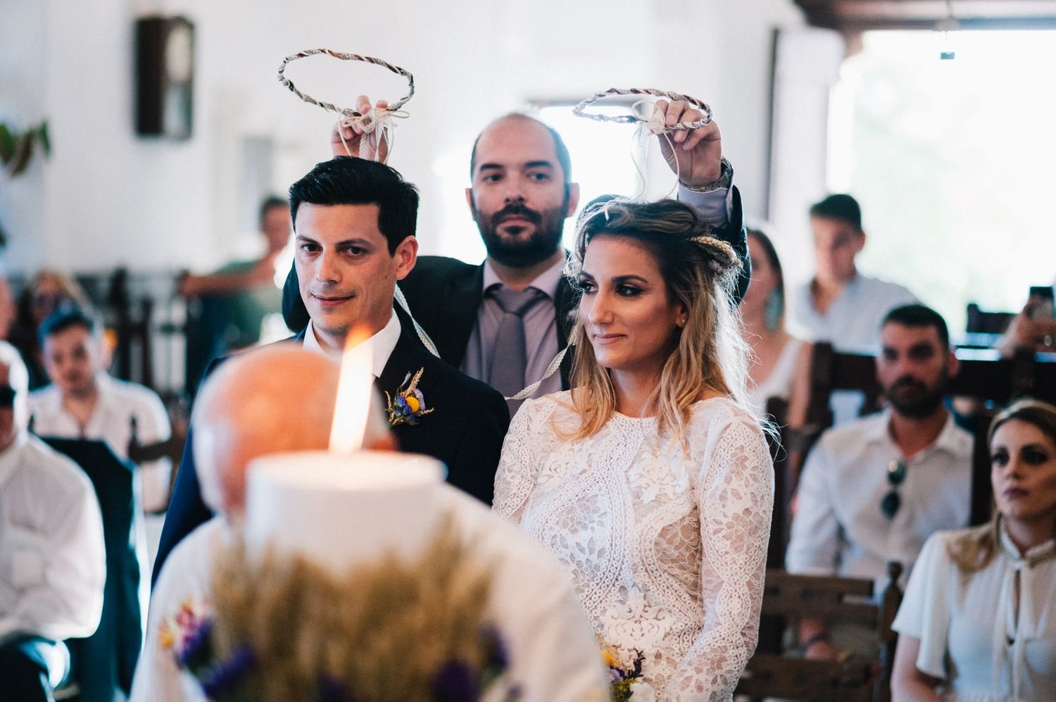 Wedding ceremony with crowns being held over couple during traditional Greek Orthodox service.