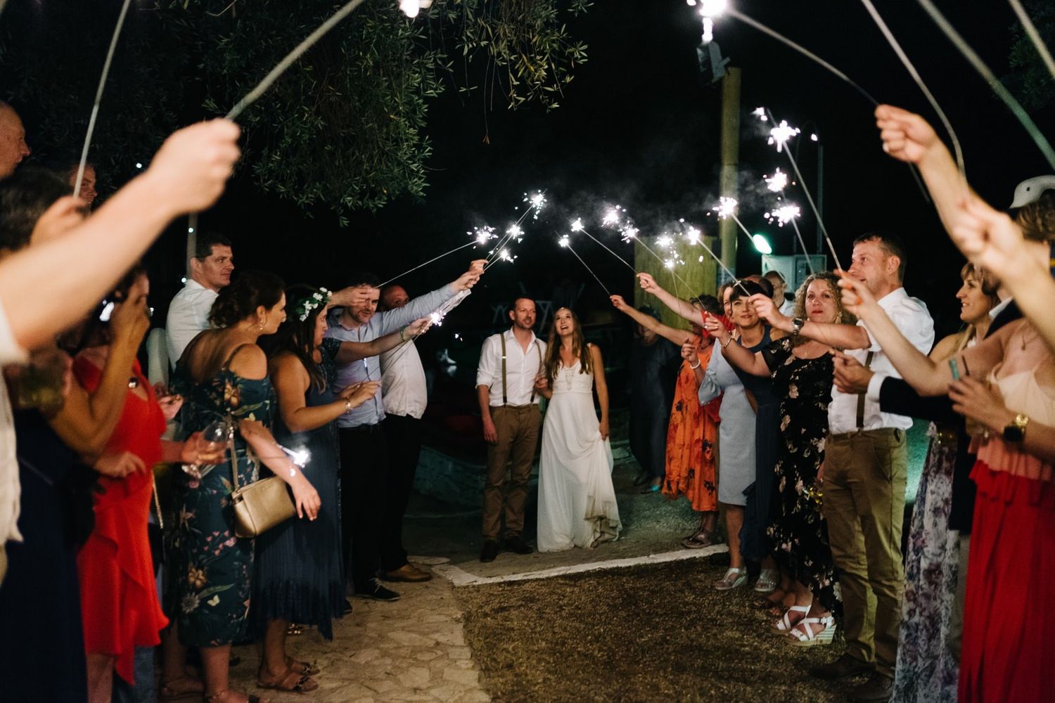 Wedding guests holding sparklers create a magical tunnel of light for the newlyweds at nighttime celebration.