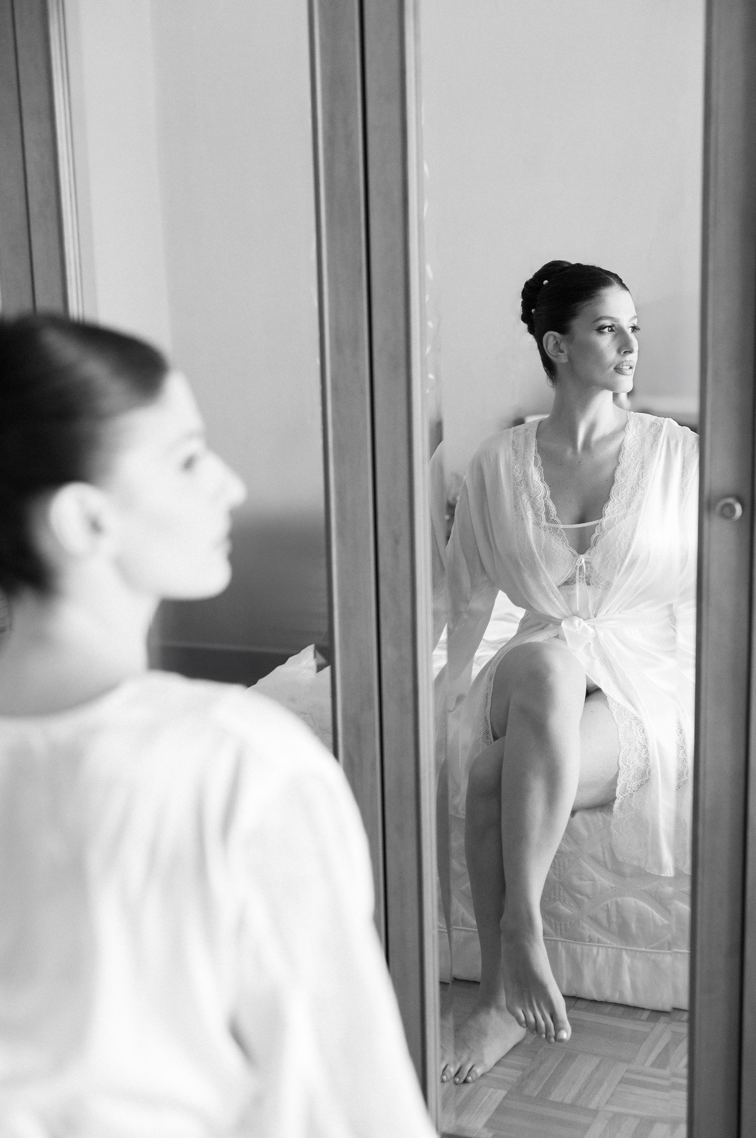 A black and white artistic portrait of a woman in a white dress gazing at her reflection in a mirror.