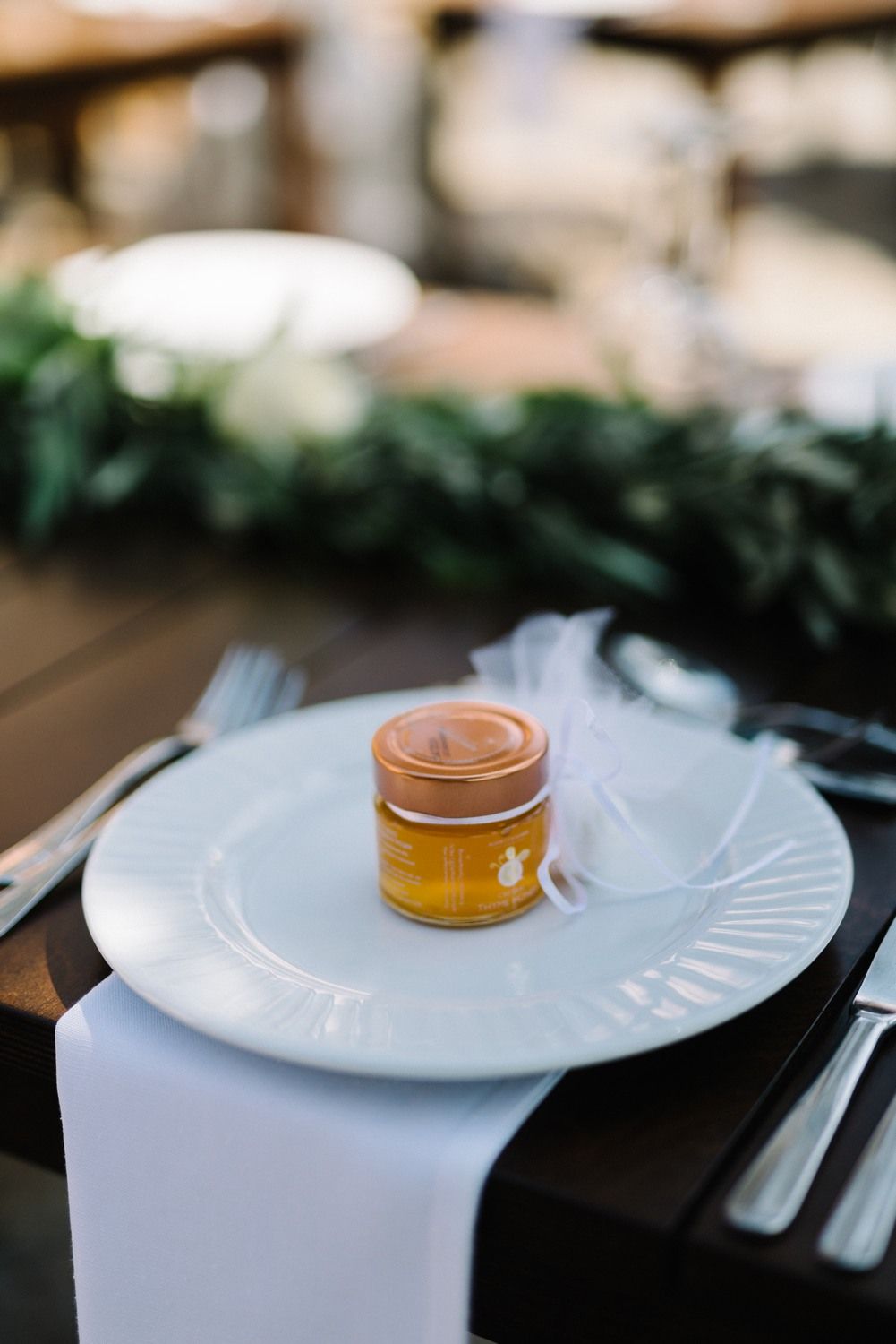 Place setting with white plate and honey jar favor on dark wooden table.