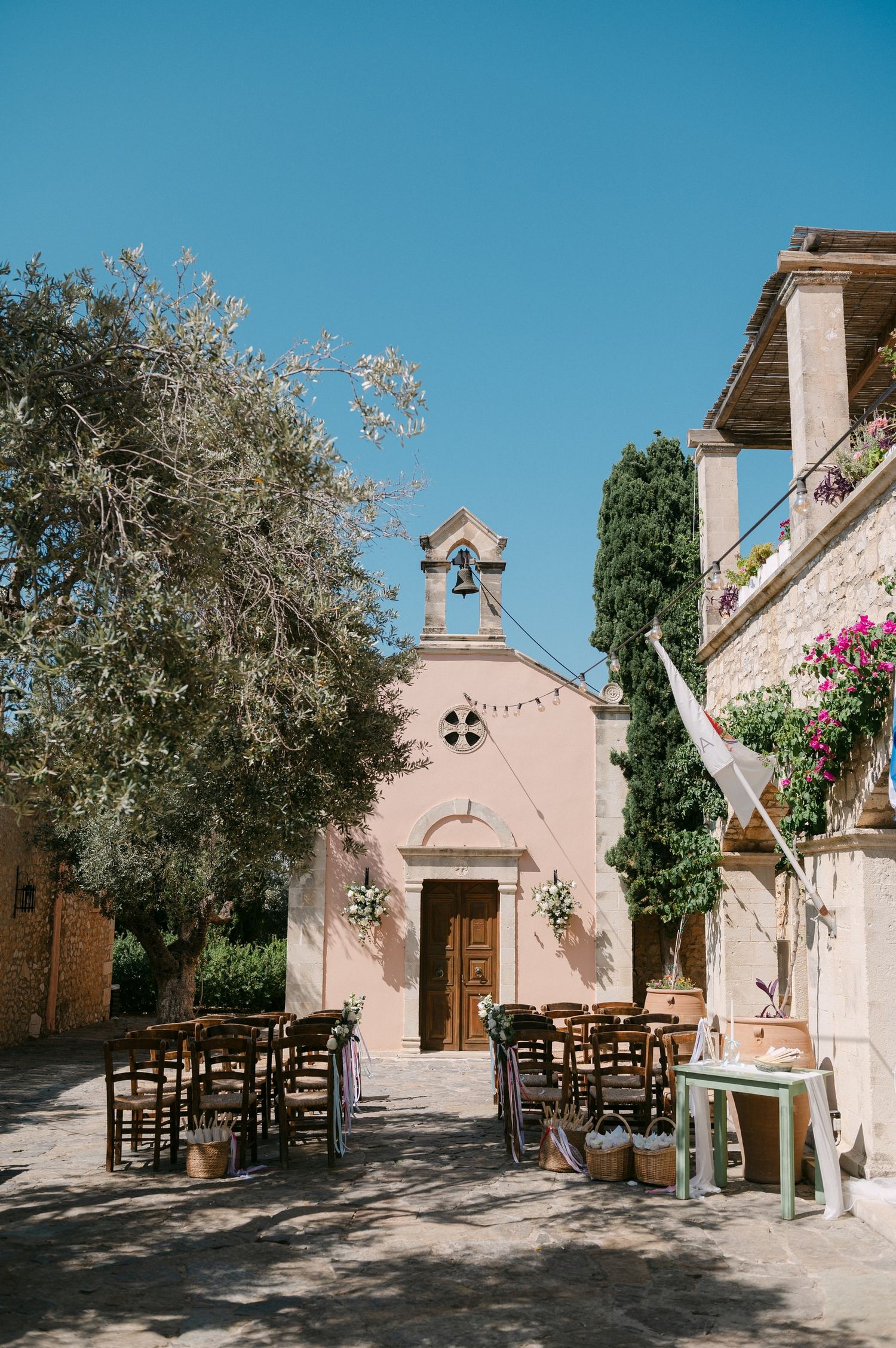 Rustic outdoor seating area with wooden chairs arranged in front of a small pink Spanish colonial style chapel on a sunny day.