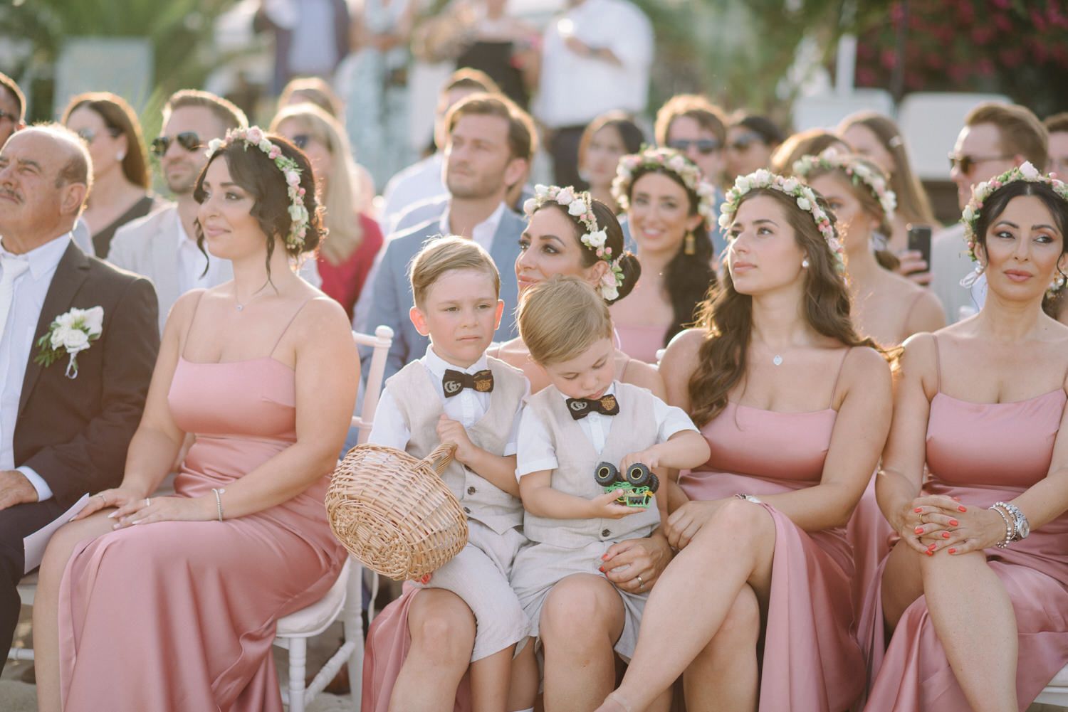 Wedding guests and bridesmaids in pink dresses seated during outdoor ceremony.