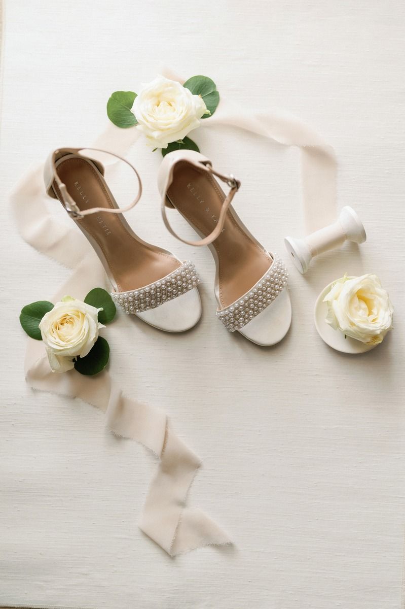 Bridal shoes with crystal details styled with white roses and silk ribbon.