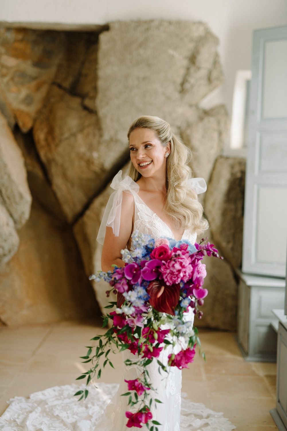 Stunning bridal portrait with colorful cascading bouquet against stone wall.