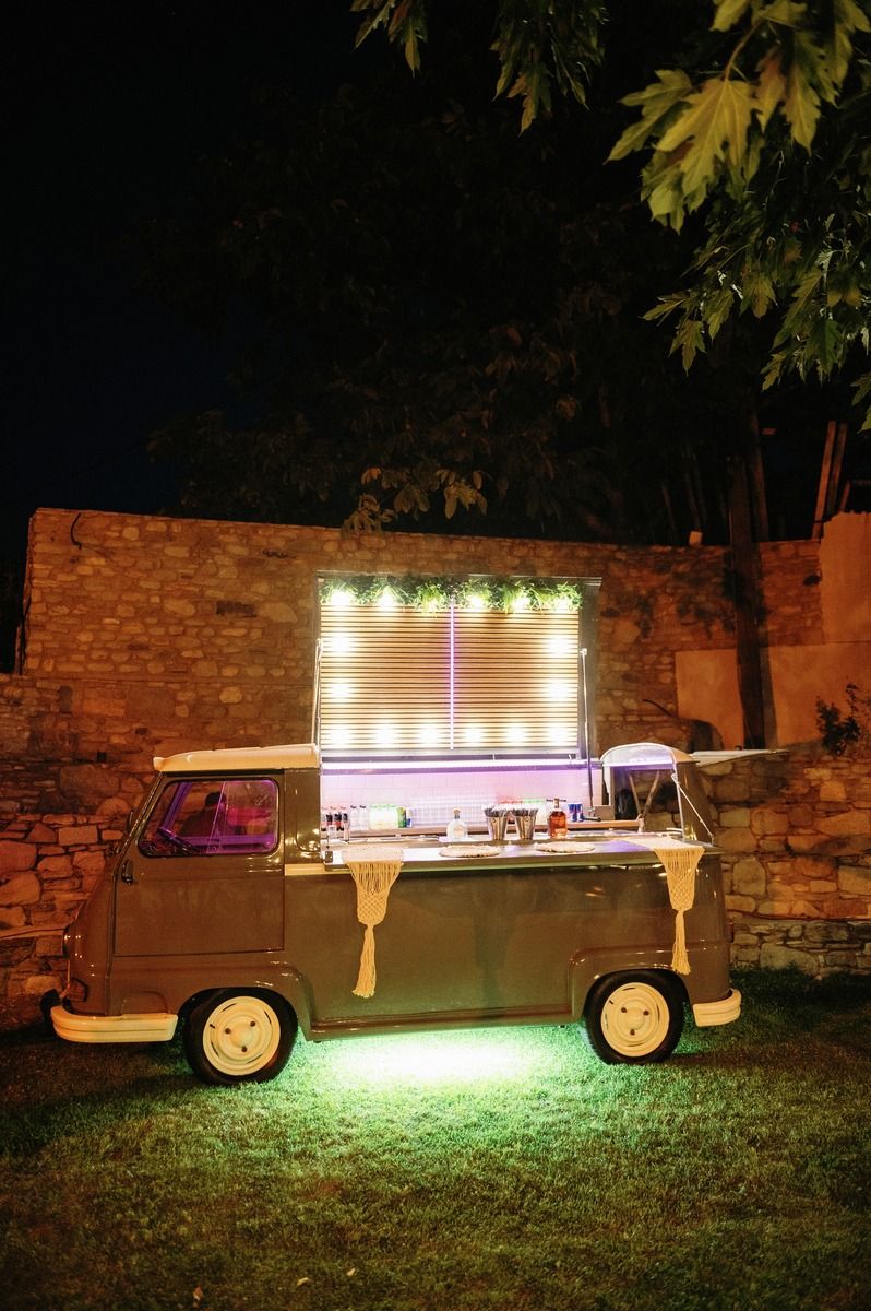 Vintage VW van converted into an illuminated mobile bar setup against a brick wall at night.