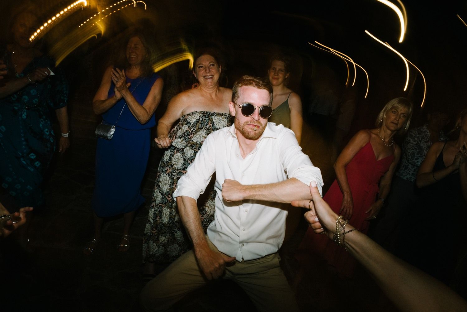 Guest in sunglasses and white shirt dancing energetically at a dark party venue.
