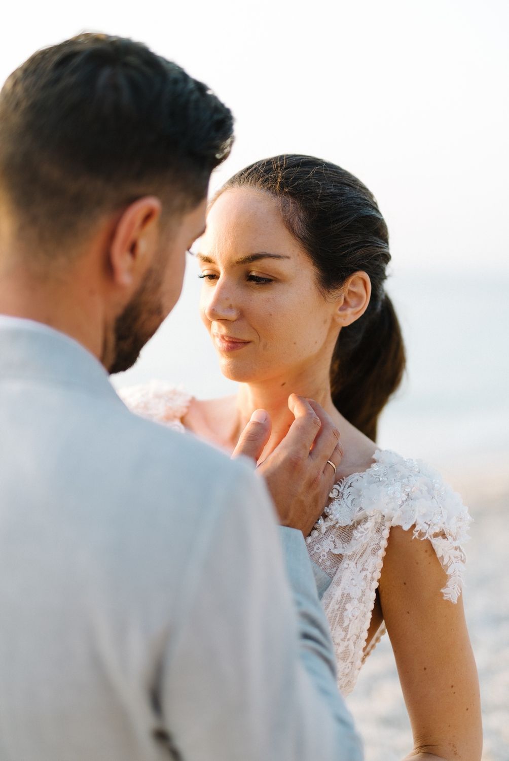 A tender moment between newlyweds captured in soft lighting on a beach.
