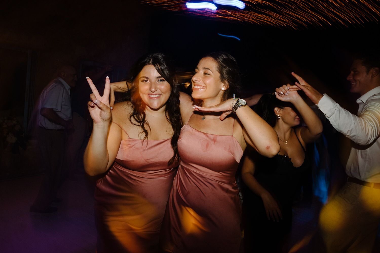 Wedding bridesmaids in matching pink dresses dance energetically on the dance floor.