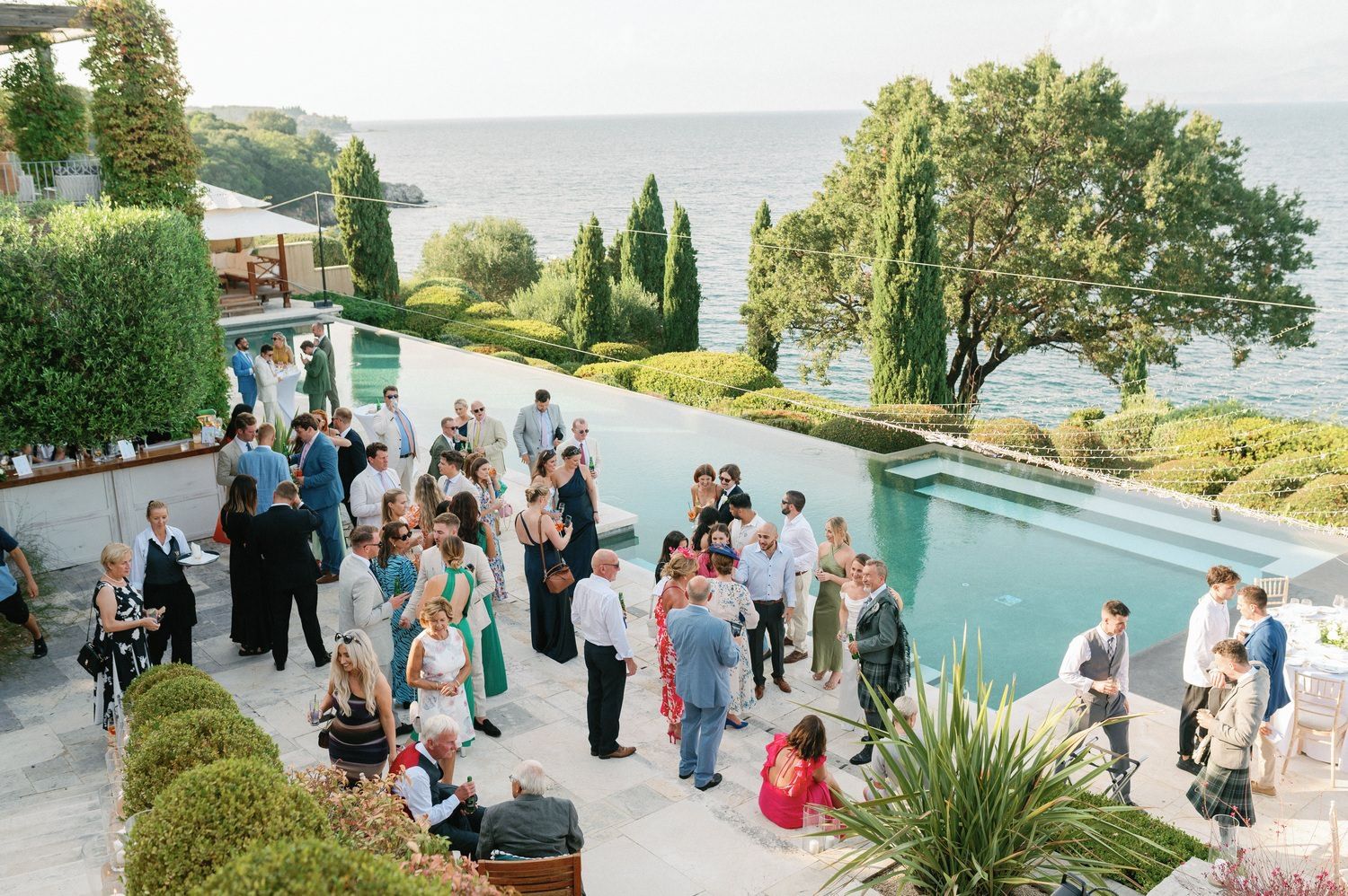 Elegant outdoor wedding reception by an infinity pool overlooking a scenic waterfront view.