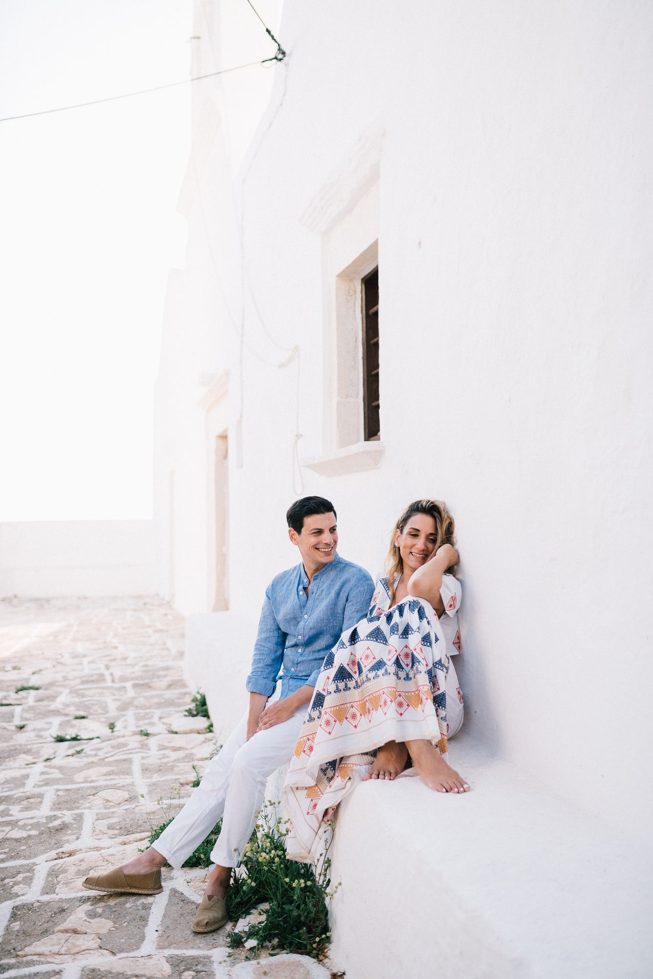 Casual couple relaxing on white Mediterranean steps during a sunny afternoon.