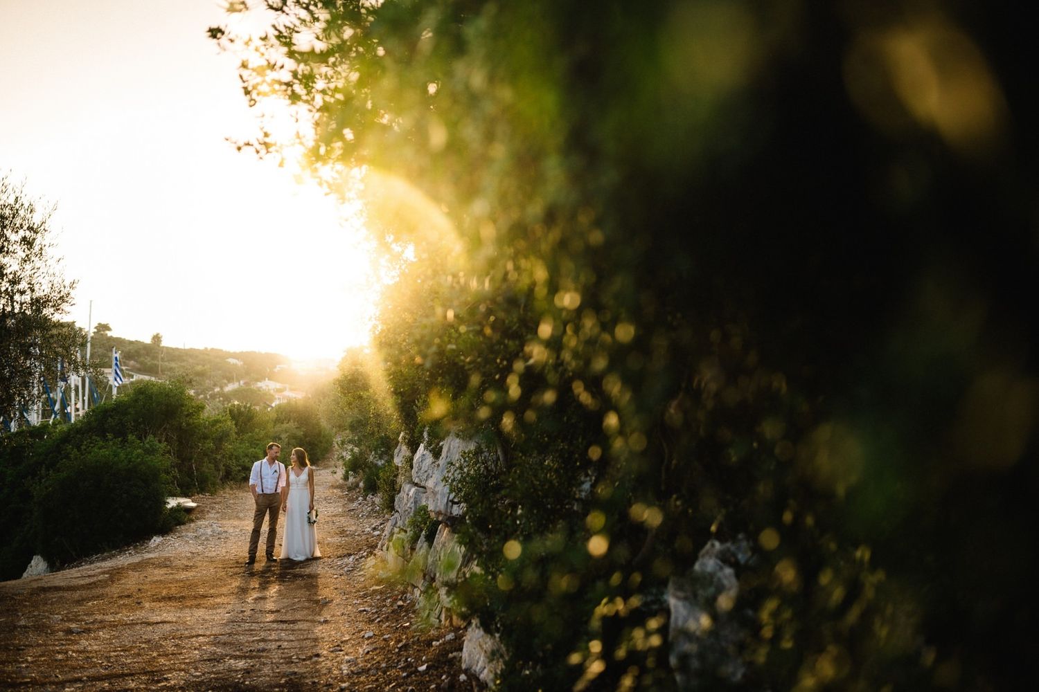 Distant shot of wedding couple walking along scenic path during sunset.