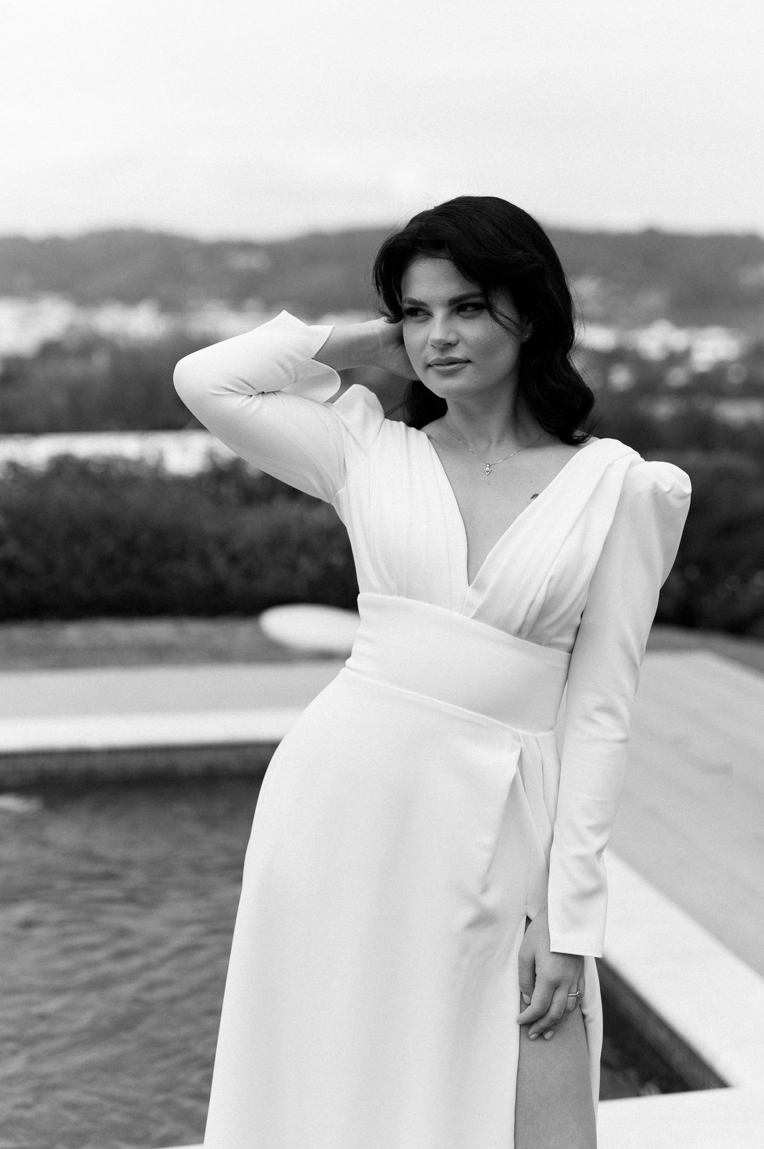 A black and white fashion photo series showing a person in a flowing white dress posing gracefully by the water.
