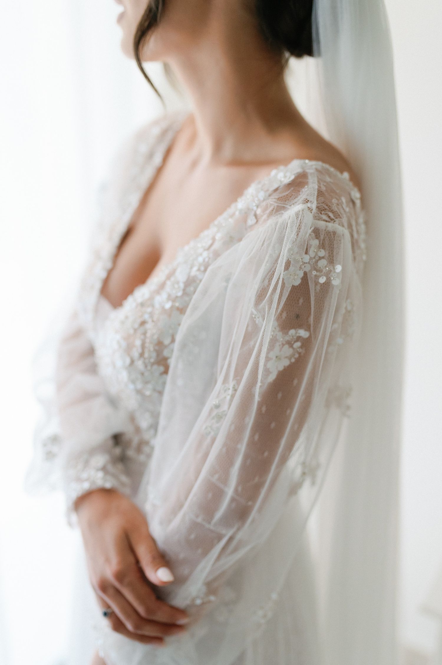 Close-up details of delicate white lace and sheer fabric on a romantic wedding dress with flowing sleeves.