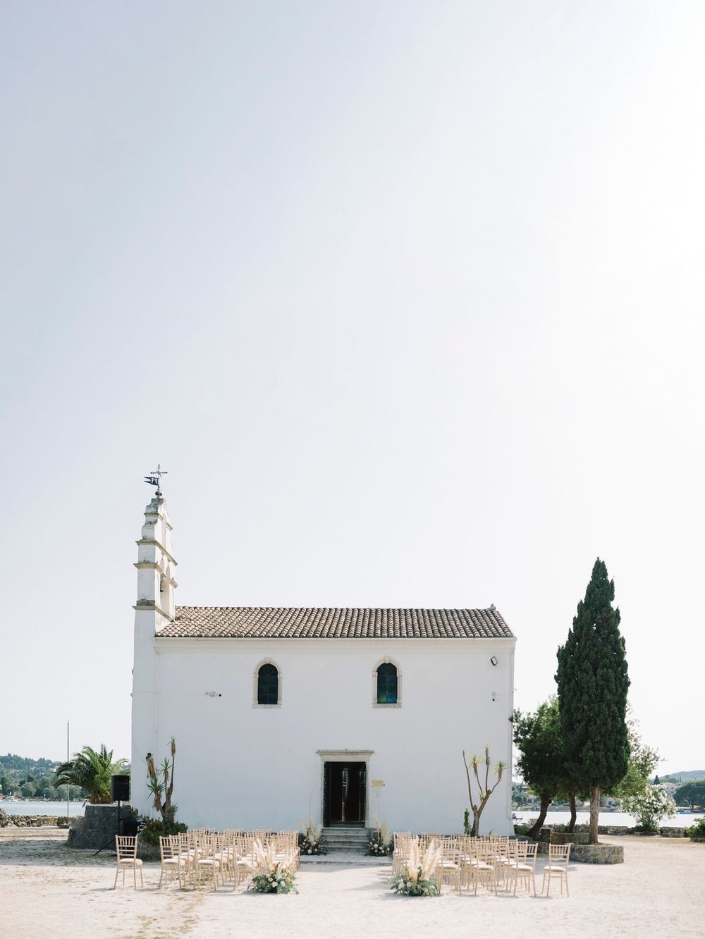 Minimalist white Mediterranean building with cypress trees and desert plants against a bright sky in panoramic view.