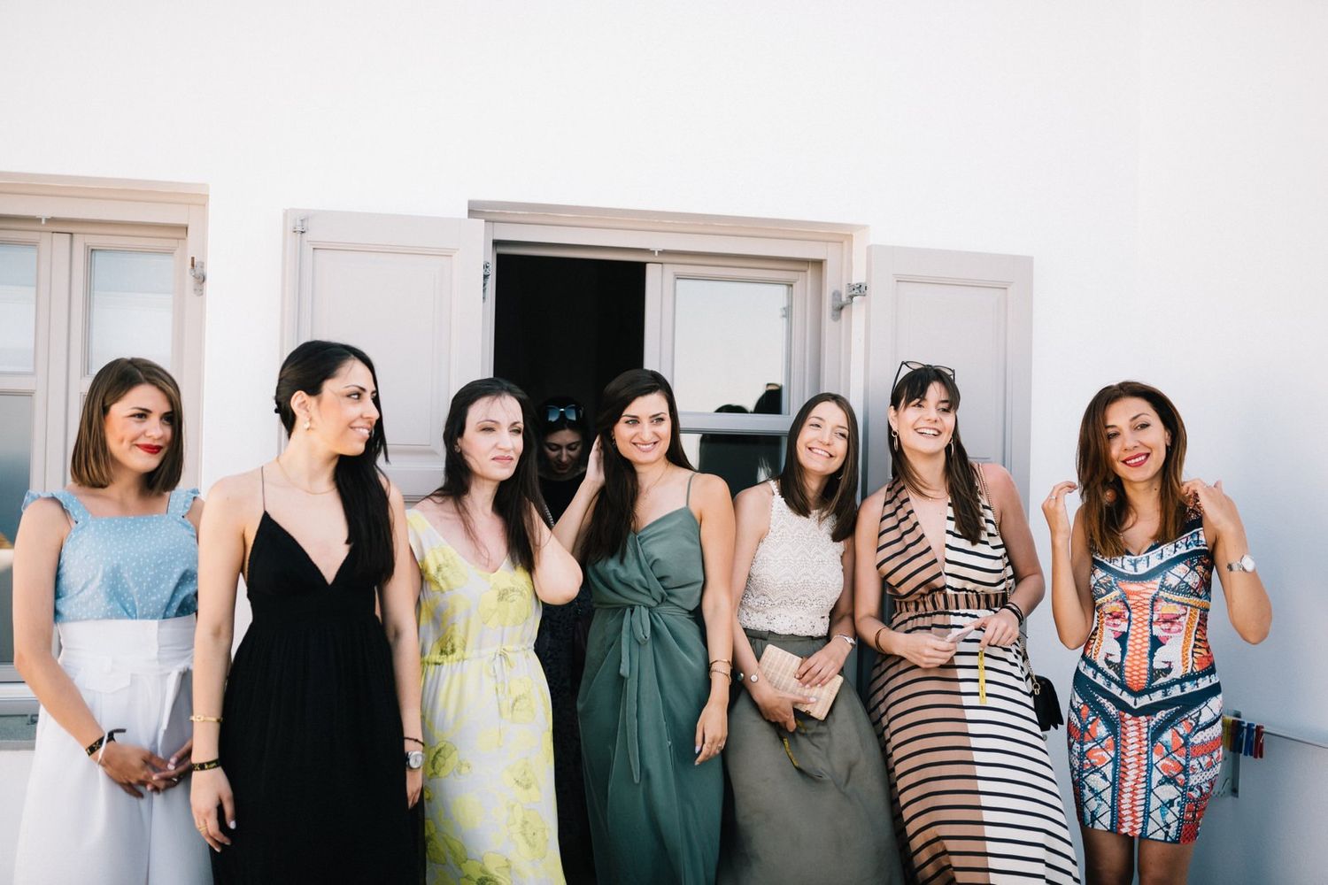 Row of bridesmaids in mix-and-match dresses posing against white wall.