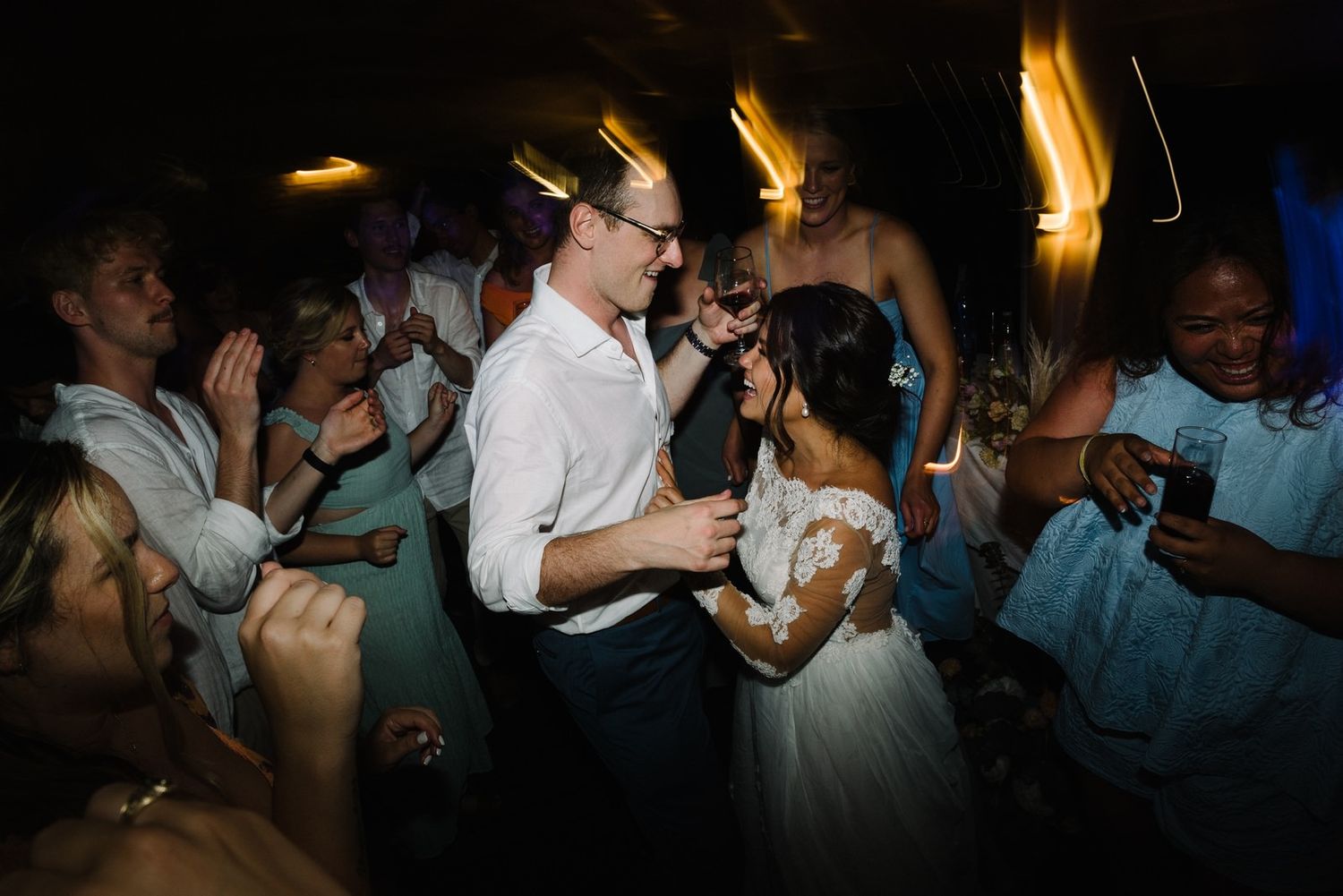 Wedding guests dance energetically on a dimly lit dance floor.