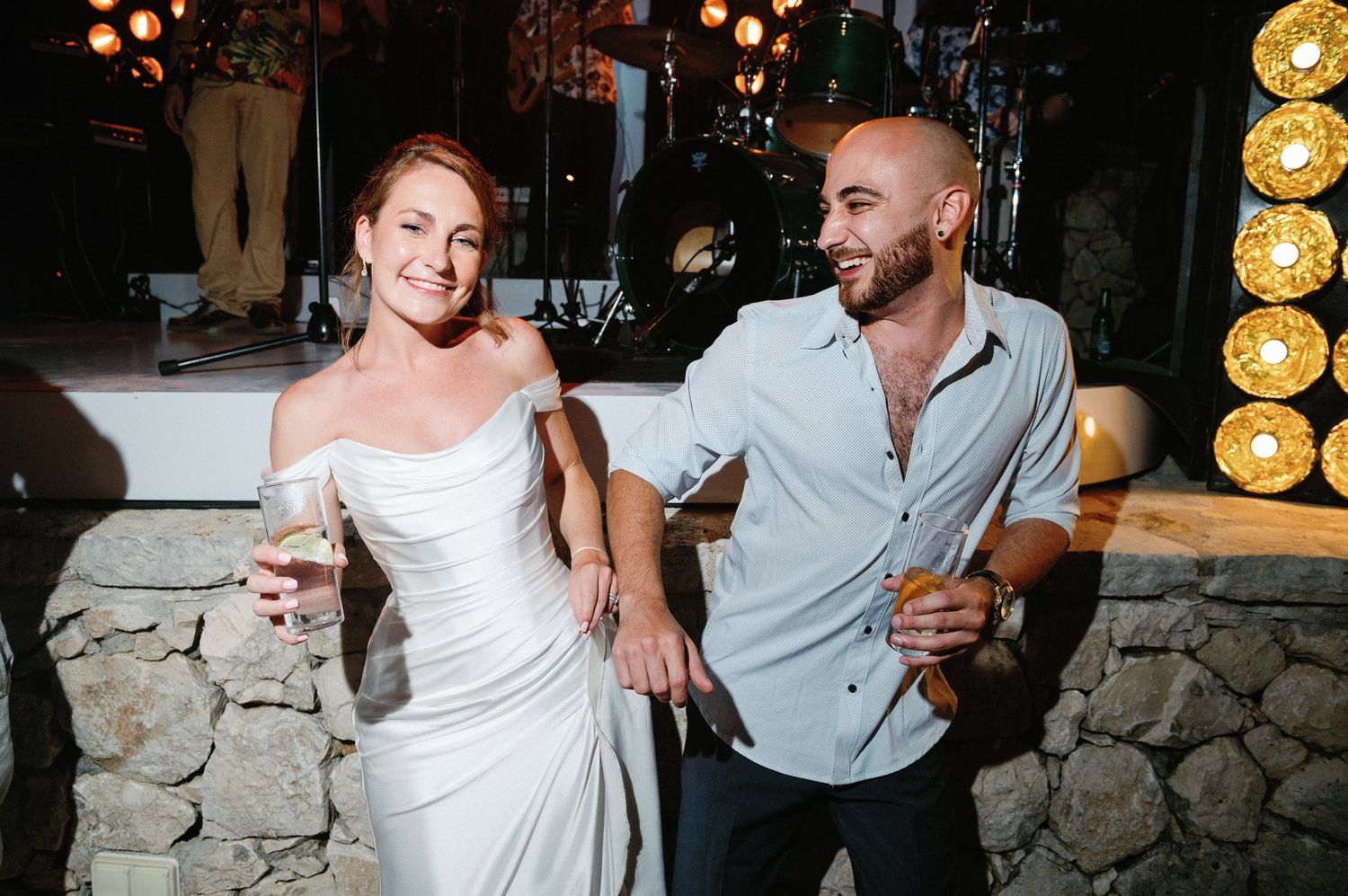 Wedding couple sharing drinks and laughing together at outdoor reception.