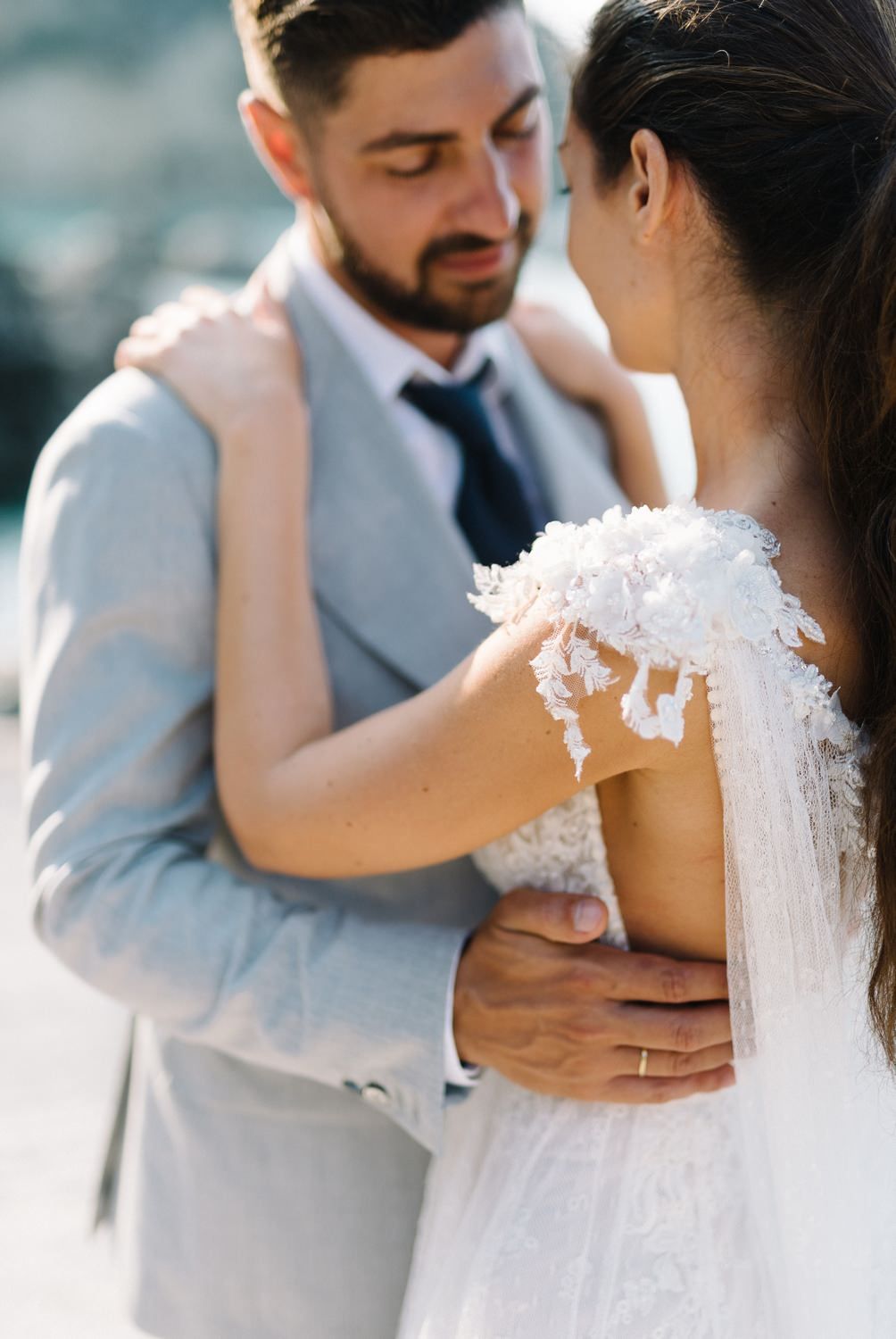 Close-up shot of a tender embrace between newlyweds in formal wedding attire by the sea.