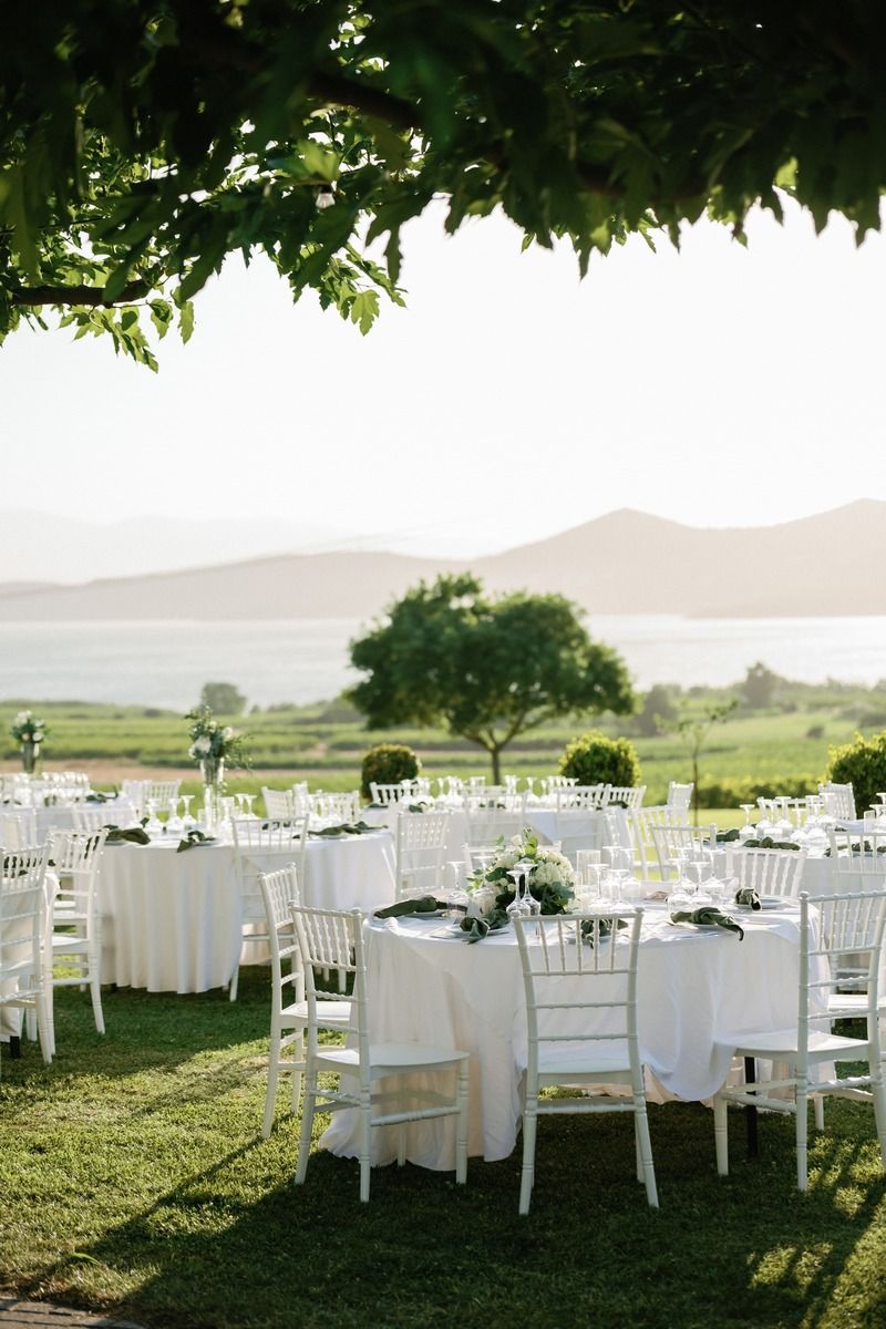 Outdoor wedding reception setup with white tables and chairs against scenic mountain backdrop.