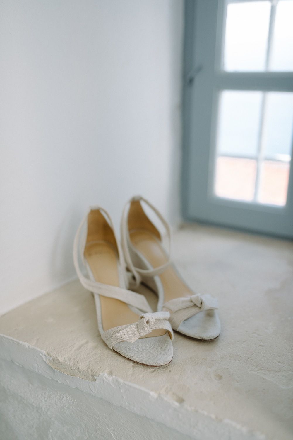 Elegant white bridal shoes positioned on a stone ledge near a window.
