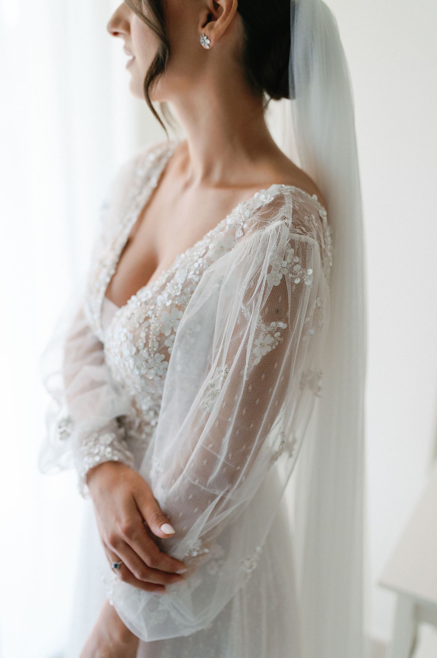 Close up of an elegant wedding dress with delicate lace sleeves and veil in soft natural light.