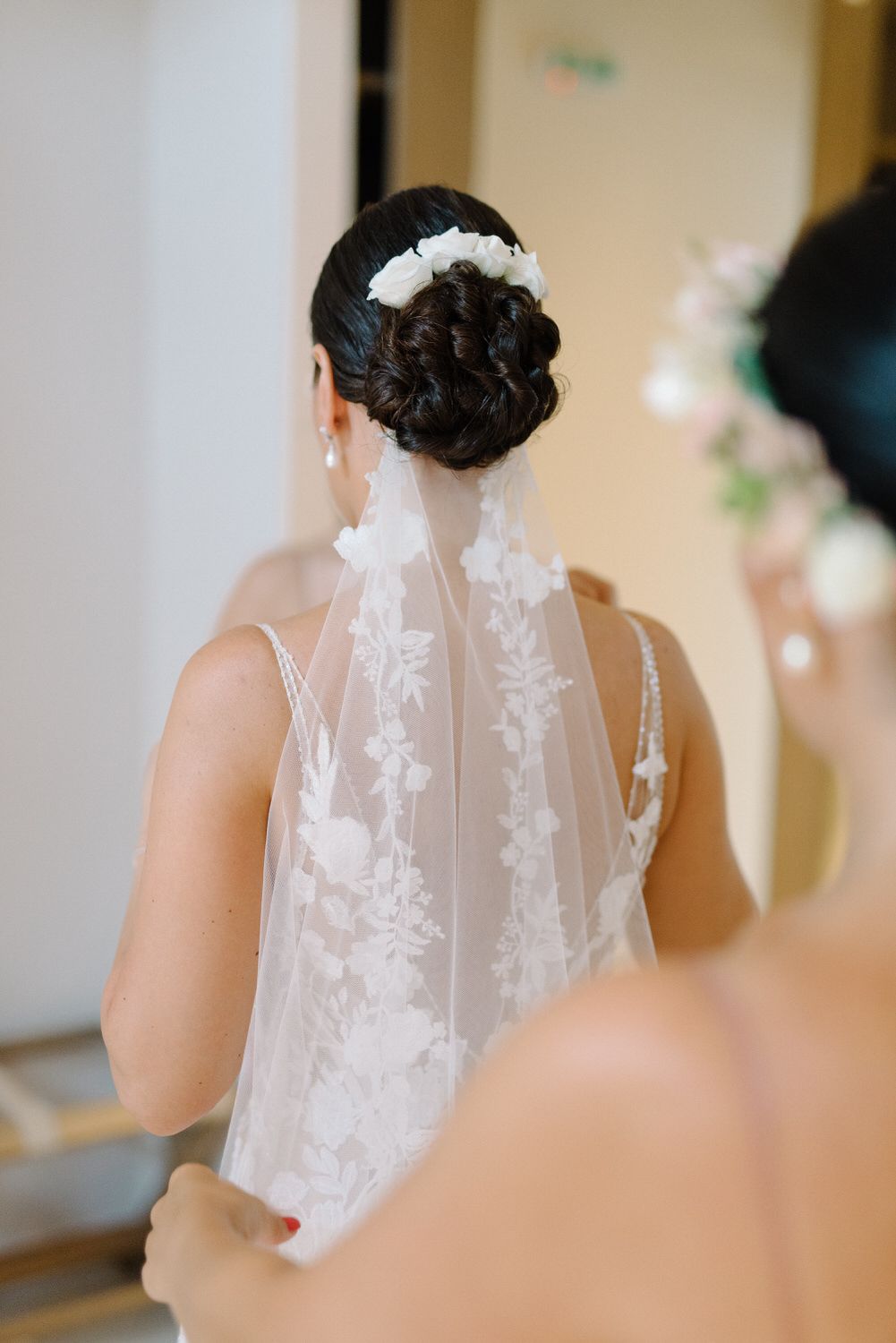 Elegant bridal updo hairstyle with white floral accessory and lace veil details.