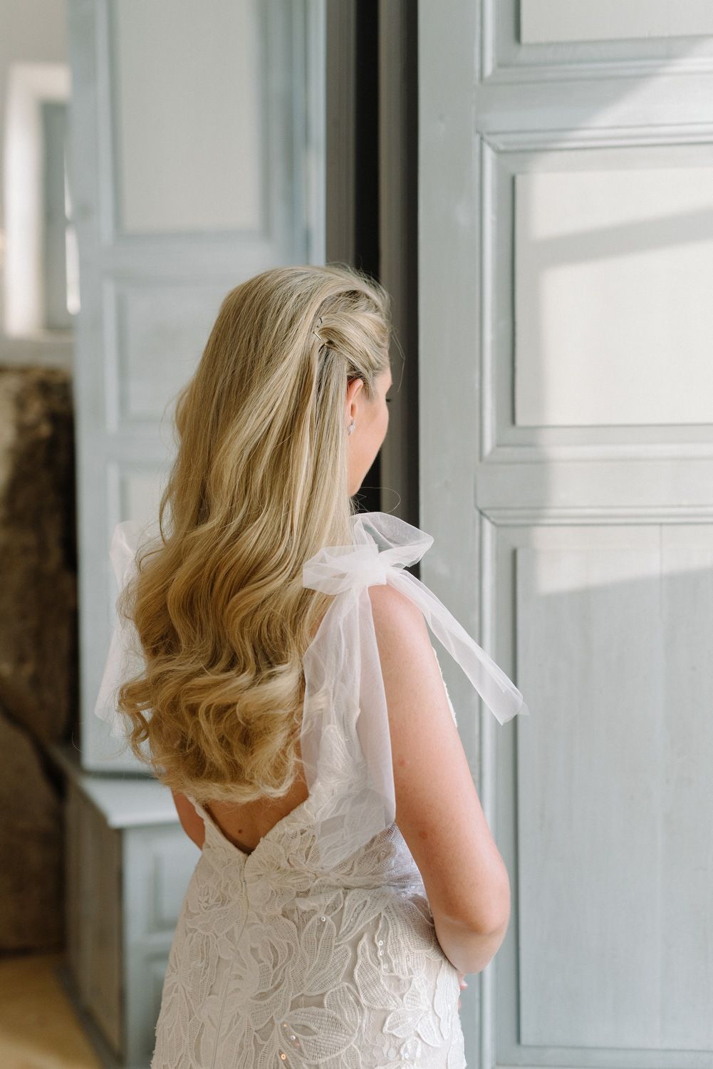 Back view of long wavy blonde hair with delicate bow detail on a white wedding dress.