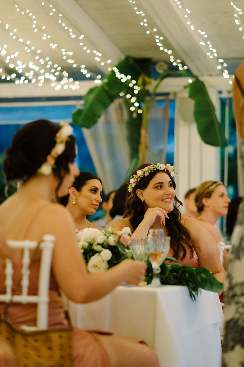 Wedding celebration under twinkling lights with tropical greenery and white floral decorations.