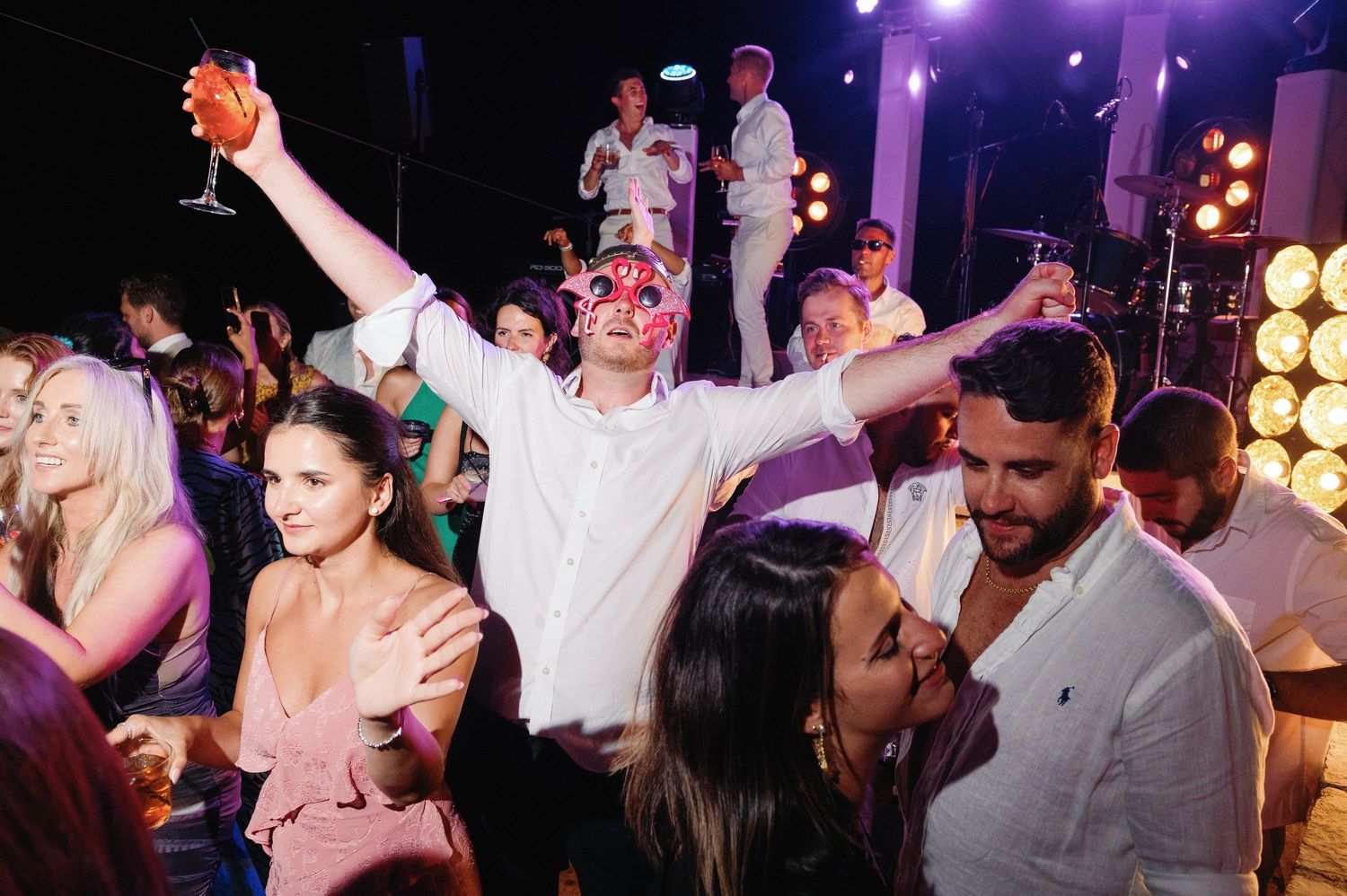 Wedding guests dancing and raising their arms in celebration on a vibrant dance floor.