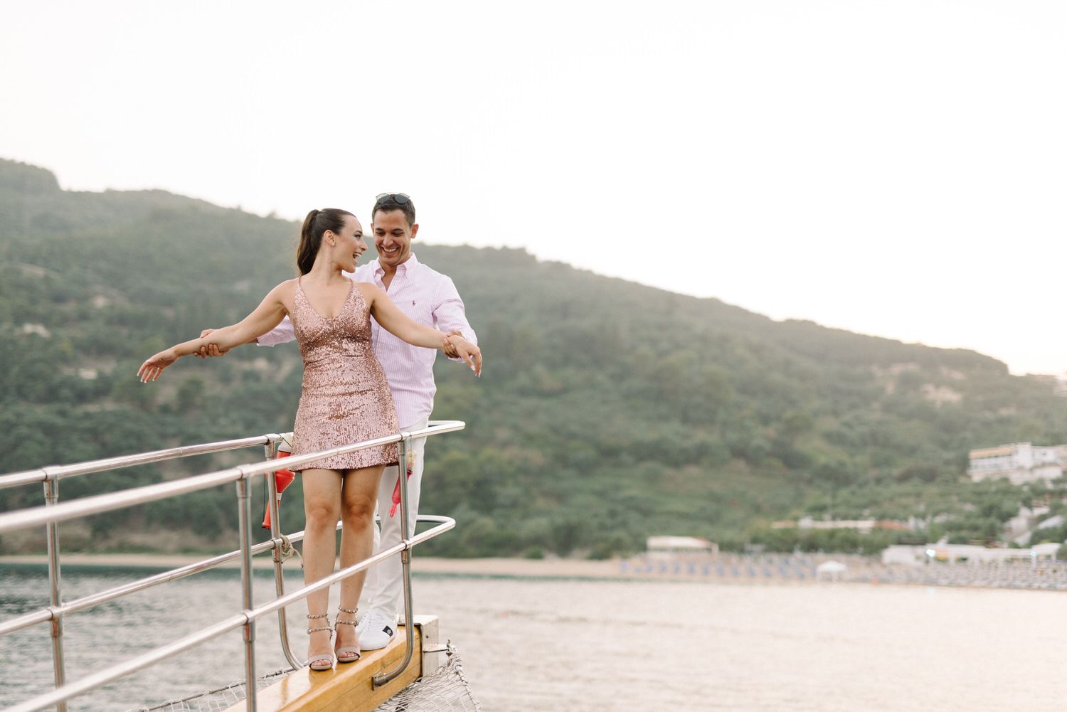 Couple in matching pink and white outfits sharing a romantic moment on a boat deck overlooking mountain scenery.