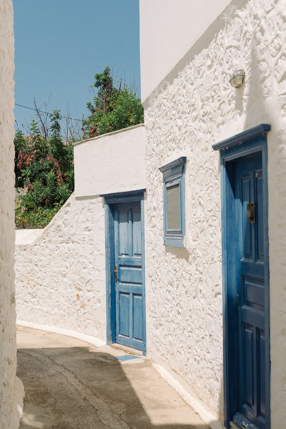 Traditional Greek architecture with white walls and blue doors along narrow path.