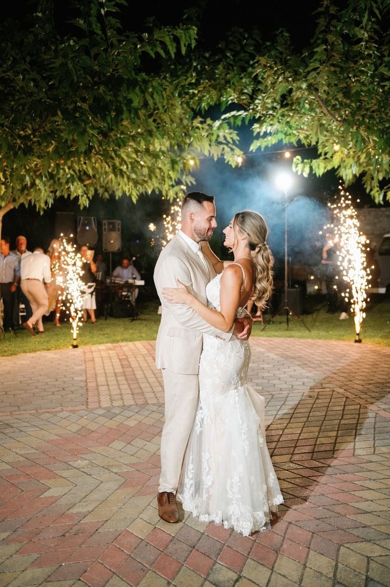 A couple shares a romantic moment on a brick patio with sparklers and string lights.