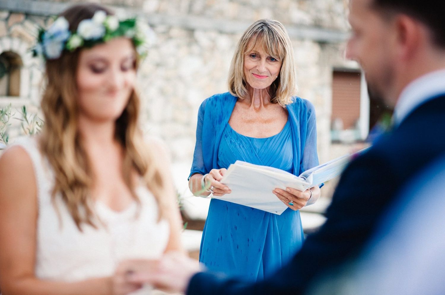 Outdoor wedding ceremony with officiant in blue dress reading from papers.