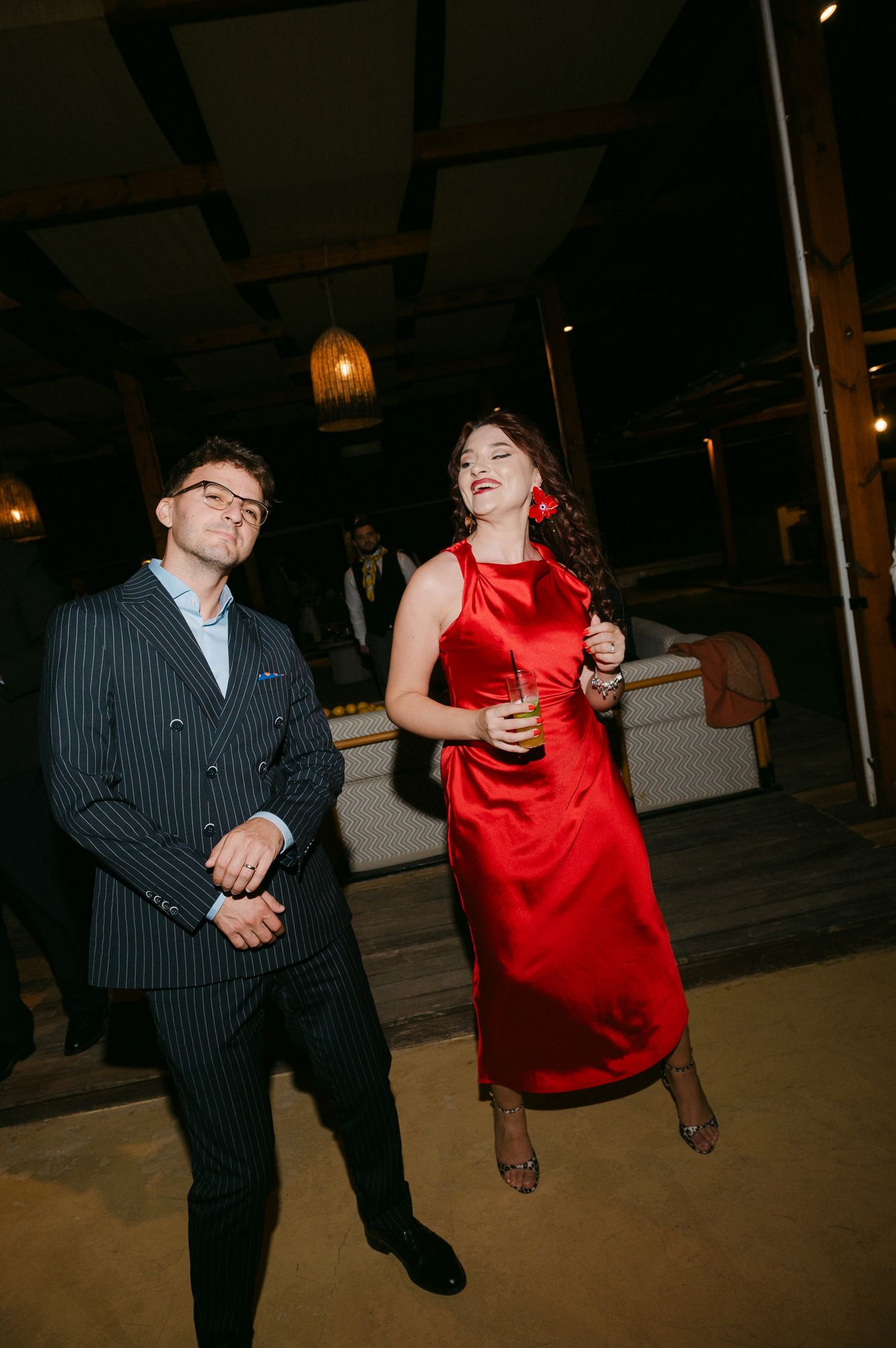 A couple dances together at a party, with the woman wearing a striking red dress and the man in a pinstriped suit.