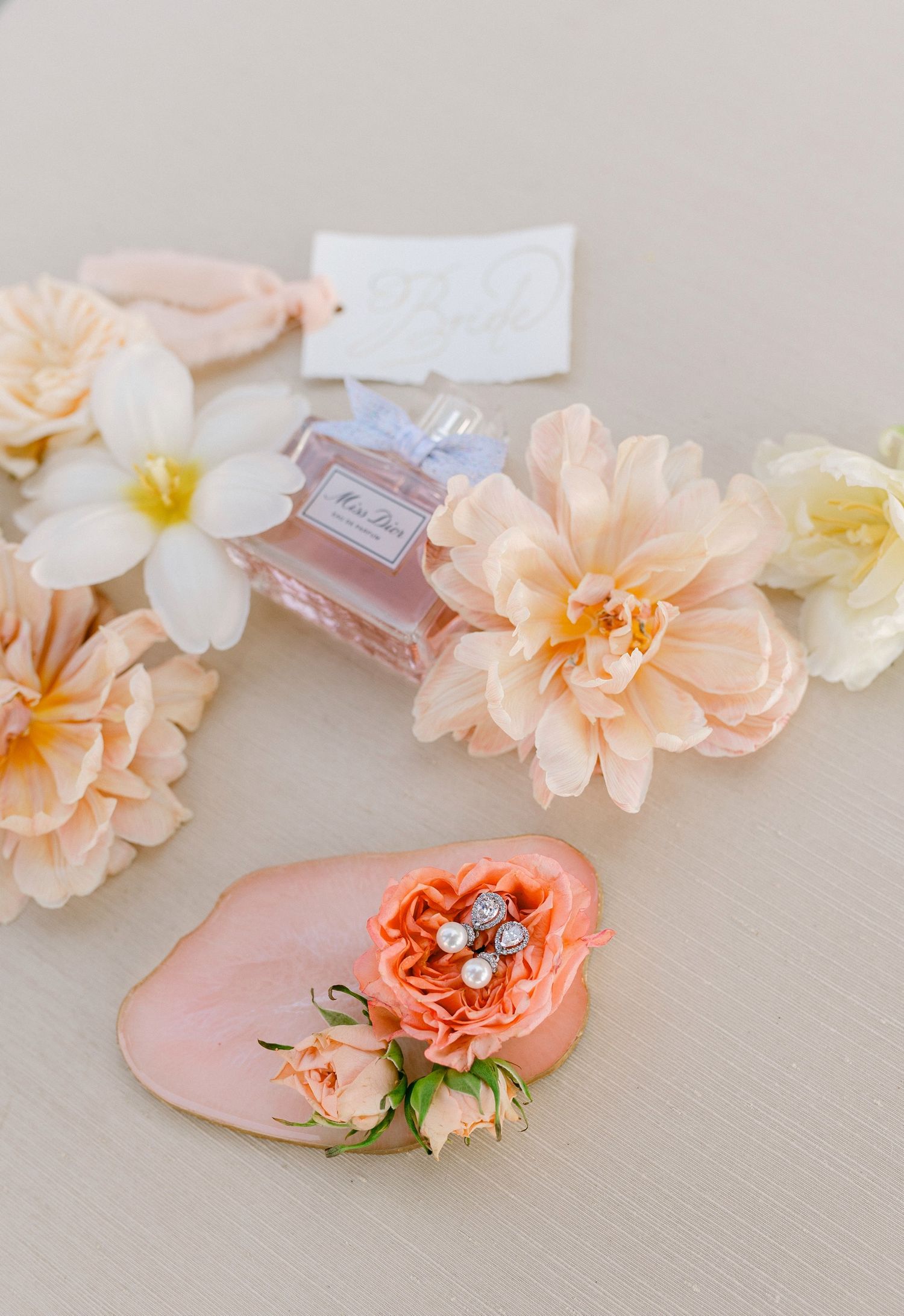 Delicate peach and coral flowers arranged with a perfume bottle on a light beige surface, creating a romantic composition.