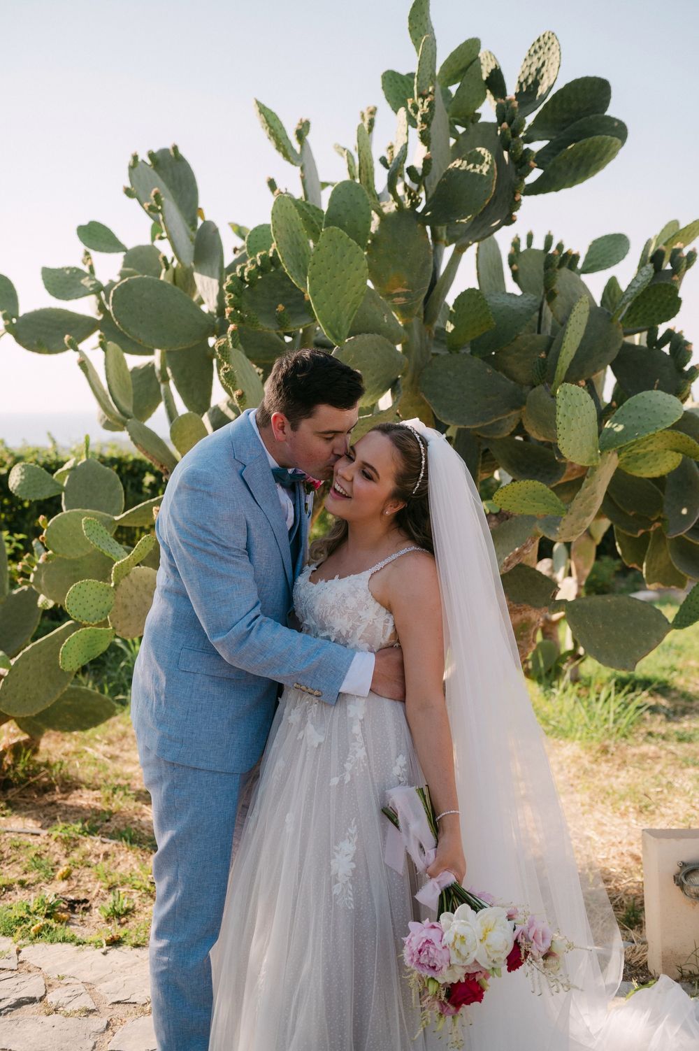 A couple shares an intimate moment among desert cacti and greenery on their wedding day in Agreco Farms, Crete