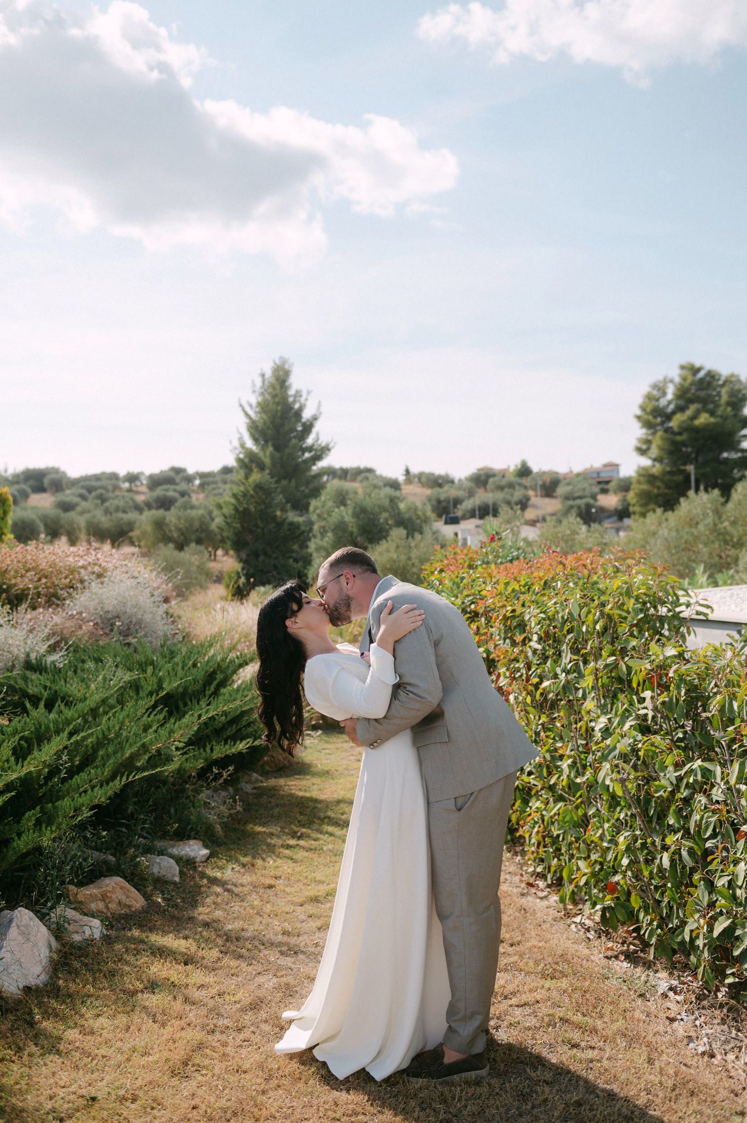 A couple poses together in a sunflower field on a bright summer day with blue skies overhead.