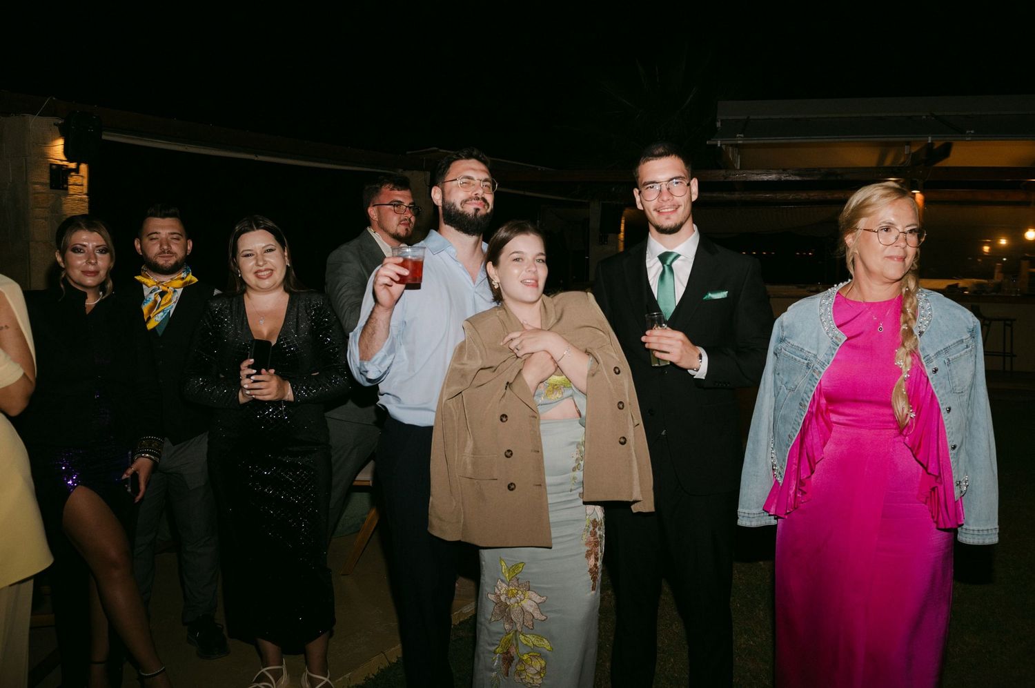 A group of people gathered in a dimly lit room wearing formal attire and casual clothing.