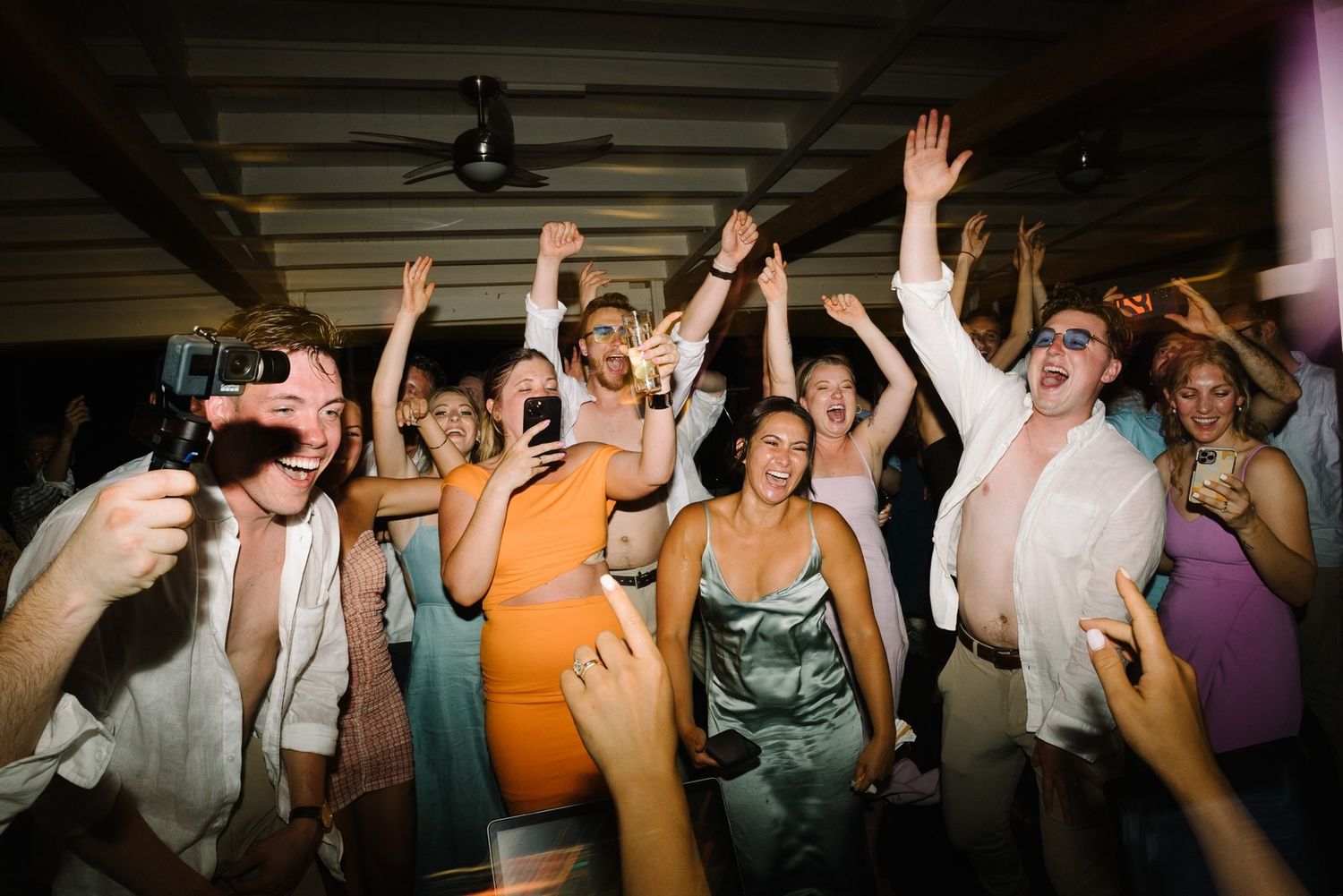 Dancing party guests raise their hands in celebration at a wedding reception.