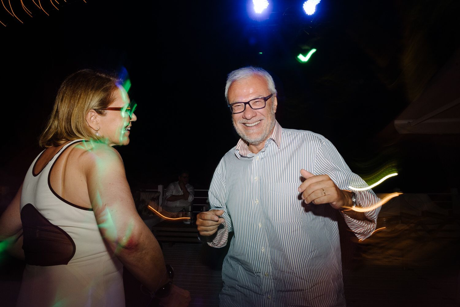 Wedding guests dancing and enjoying themselves at a reception with colorful lighting.