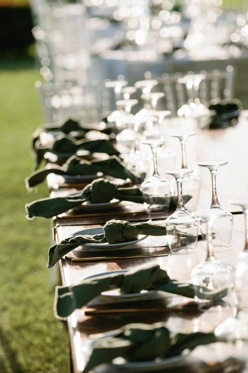 Elegant table settings with folded napkins and wine glasses lined up at outdoor reception.