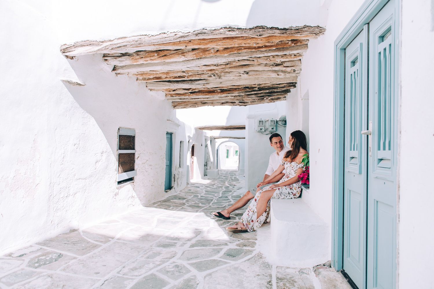 A charming whitewashed corridor with turquoise doors and rustic ceiling beams in a traditional Greek island setting.